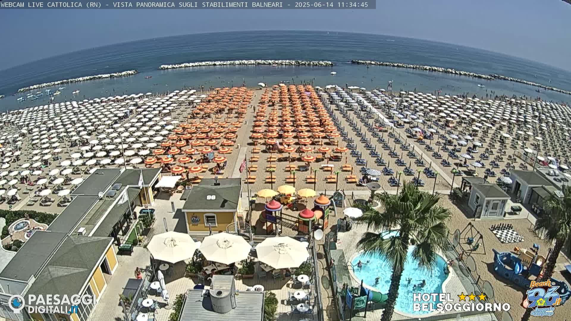 A sunny day at a crowded beach with numerous umbrellas and beach chairs, a small pool, and a playground.