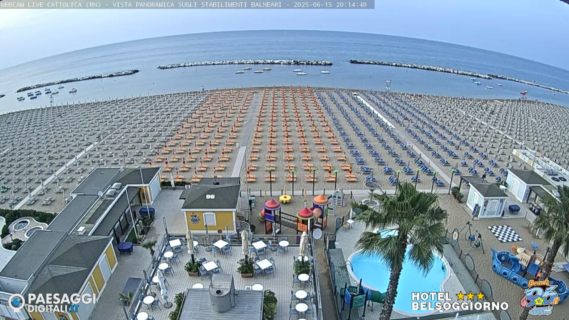 A beach with rows of lounge chairs and umbrellas is shown, next to a resort with a pool and playground; the weather appears to be clear and calm.