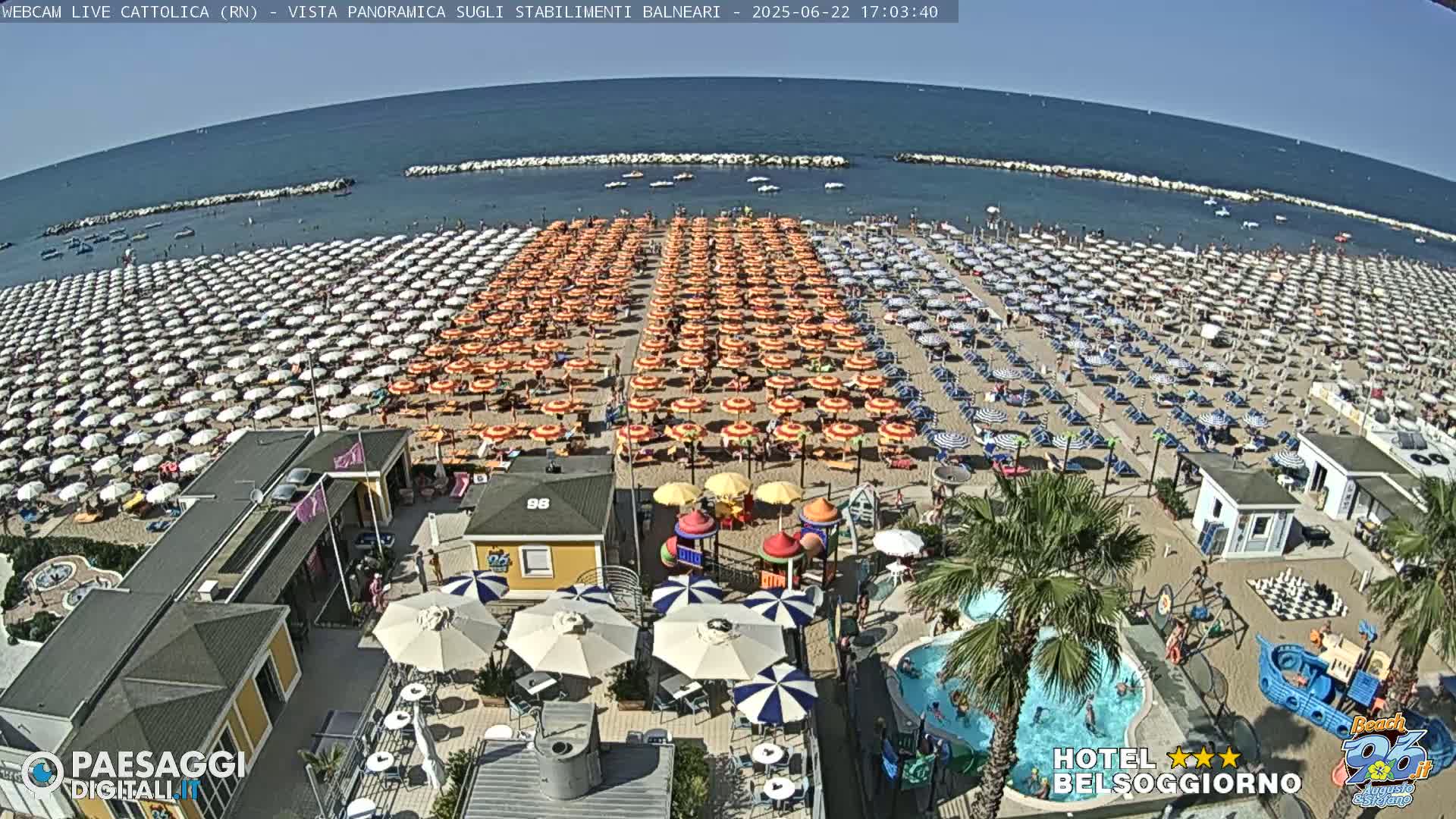 A crowded beach with many rows of colorful umbrellas under a sunny sky.