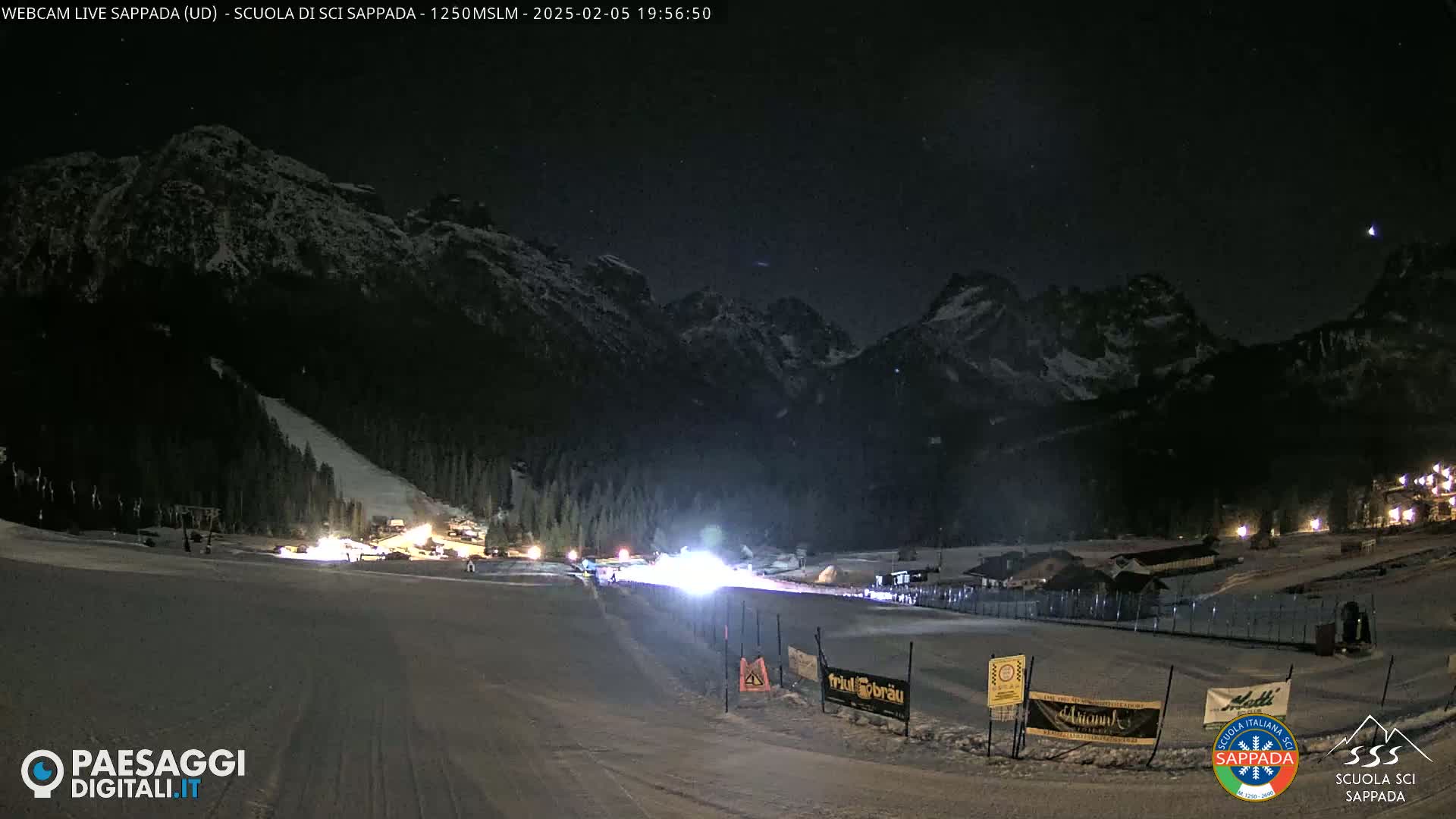A nighttime view of a snow-covered ski slope with mountains in the background under a clear, starry sky.