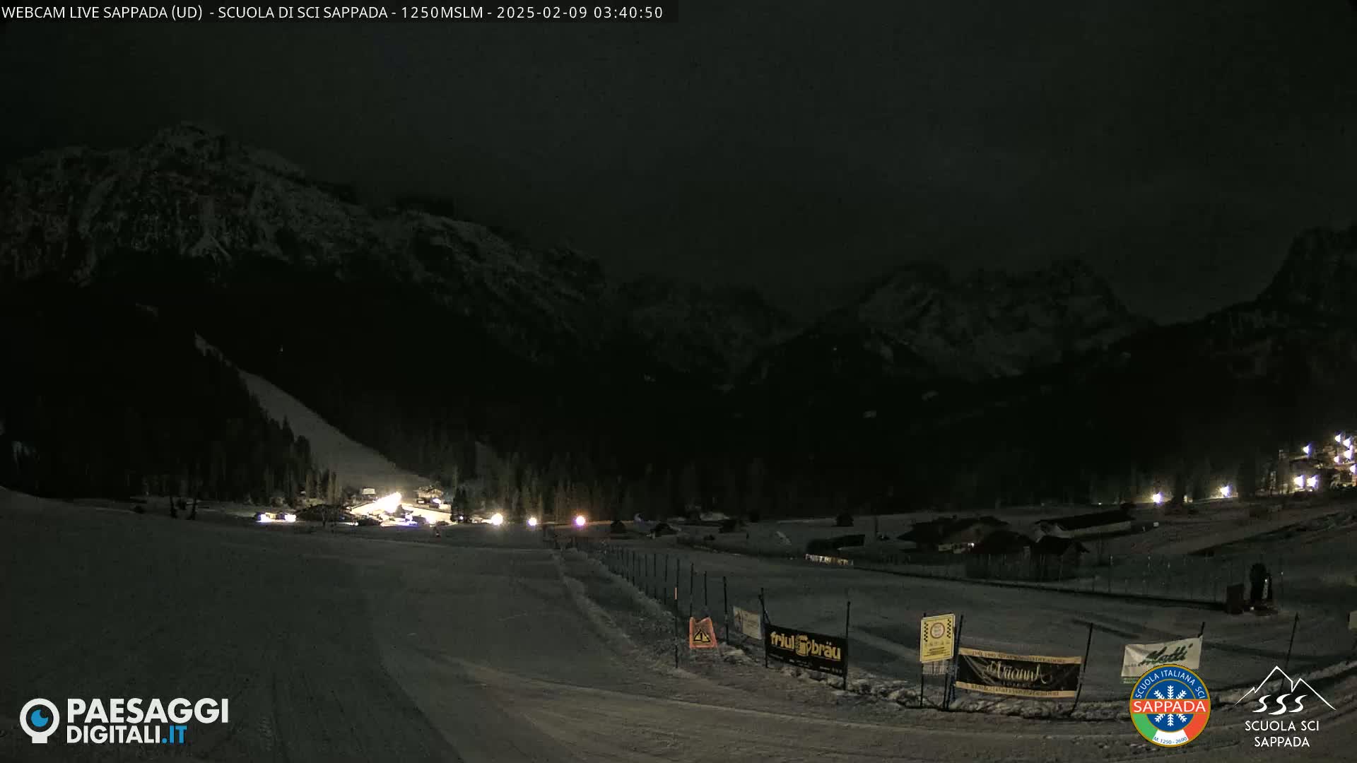 A nighttime view of a snow-covered ski slope with mountains in the background under a dark sky.