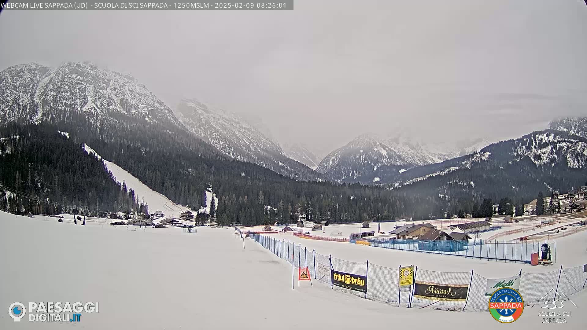 A snow-covered ski slope and surrounding snow-dusted mountains are visible under an overcast sky.