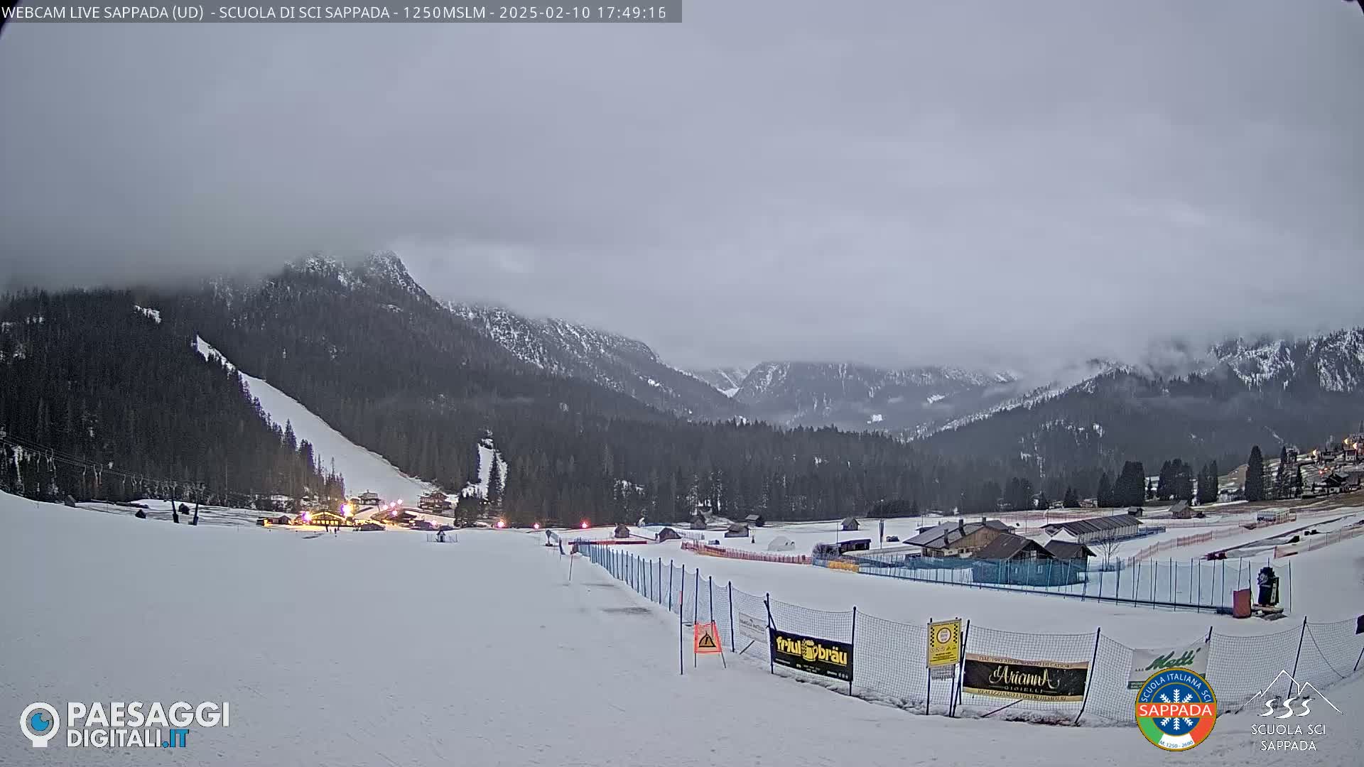 A snow-covered ski slope and surrounding mountain range are visible under an overcast sky.