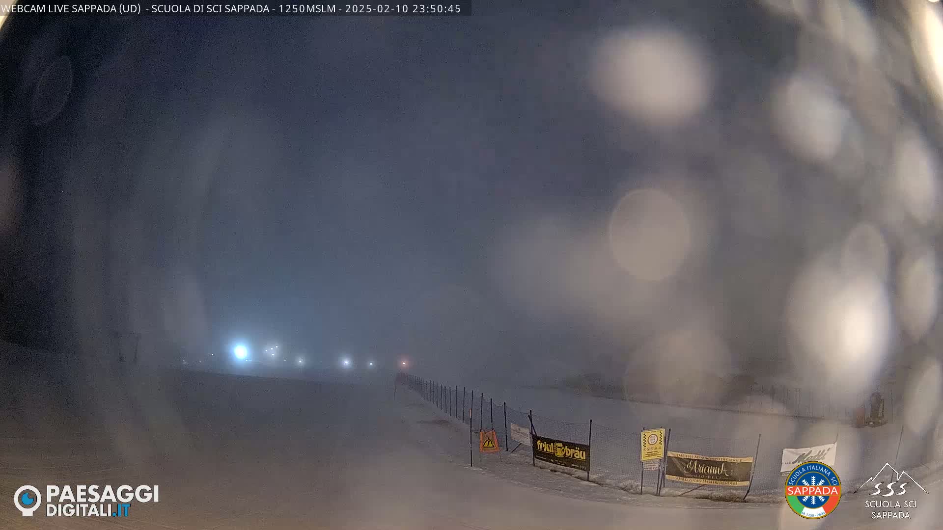 A snowy, foggy night scene shows a snow-covered path with a fence and distant lights, obscured by heavy fog.