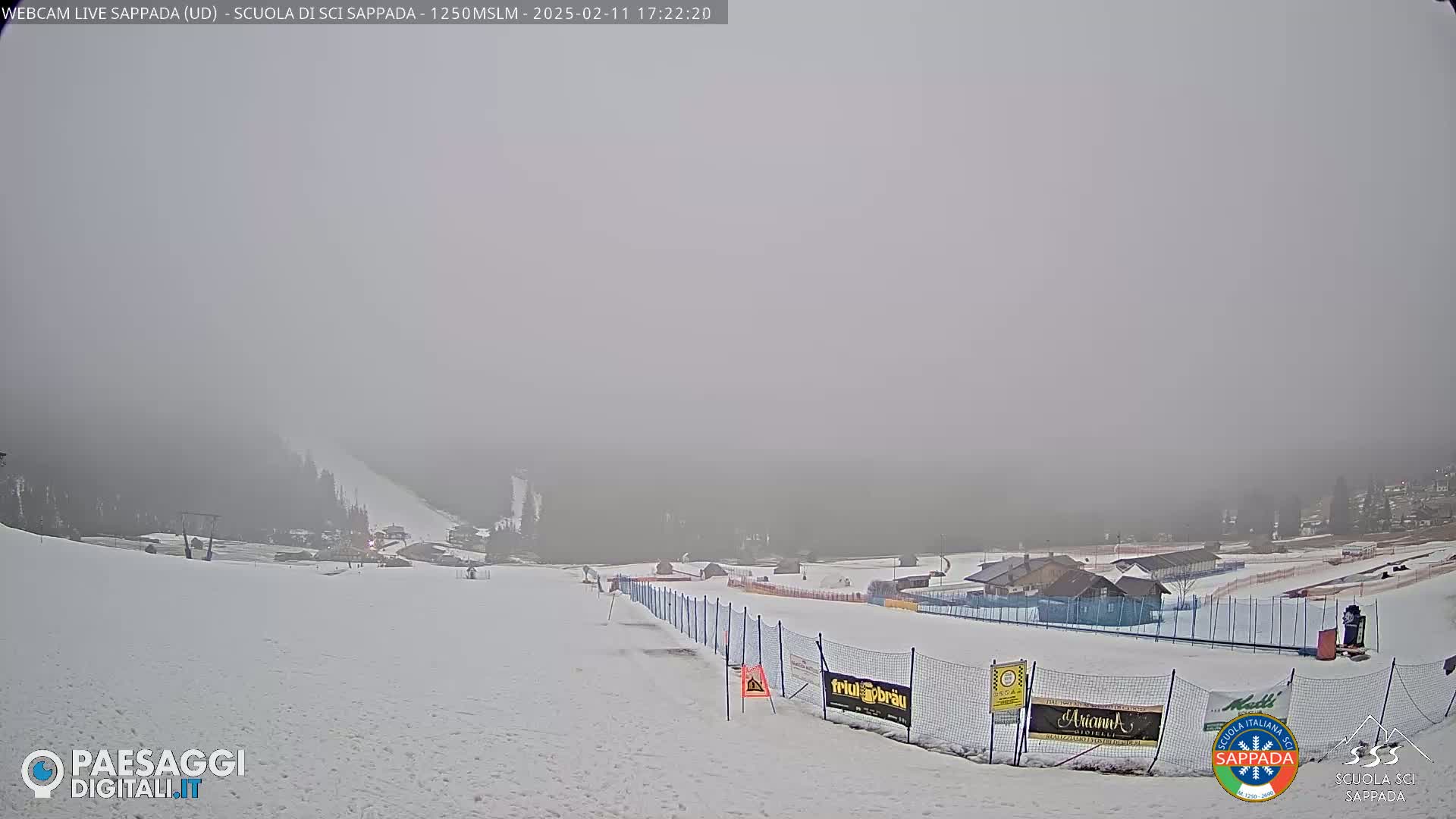 A snow-covered ski slope is visible in foggy conditions, with a few buildings and fences in the background.