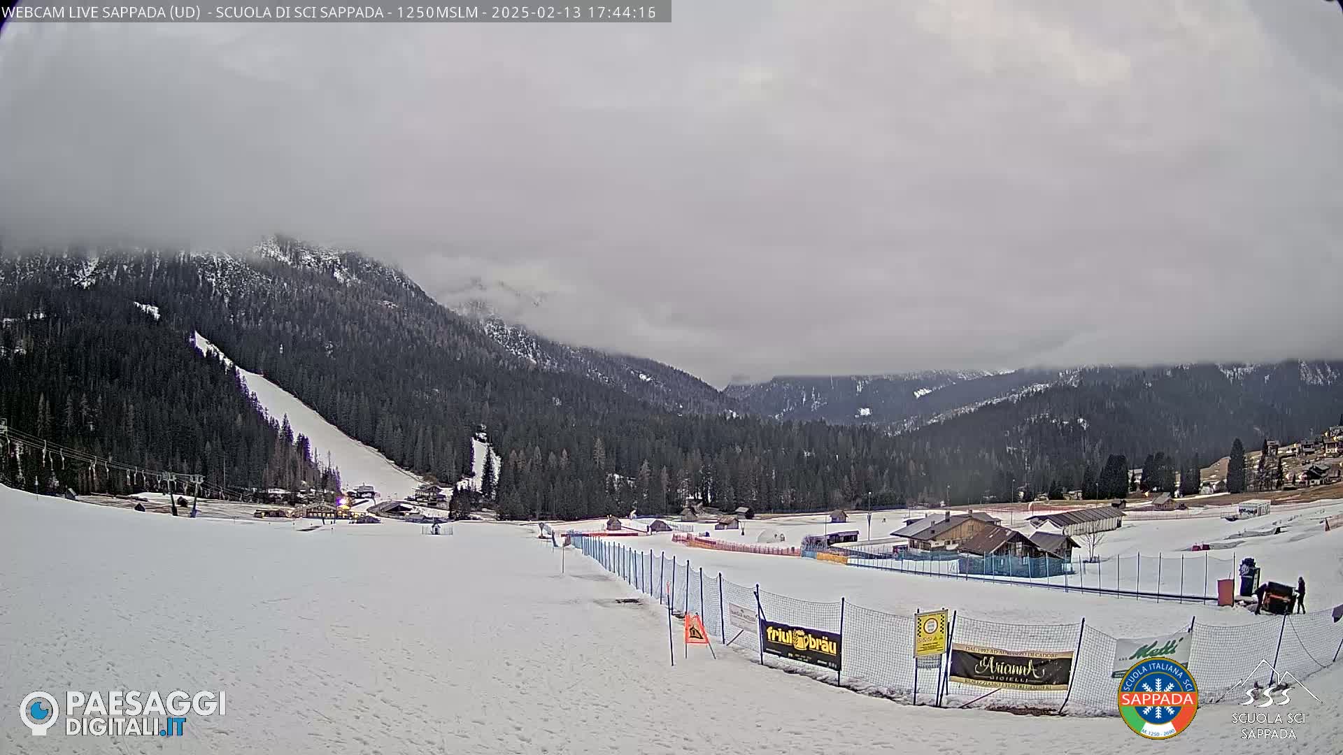A snow-covered ski slope with a ski lift and several buildings is visible under a cloudy sky.