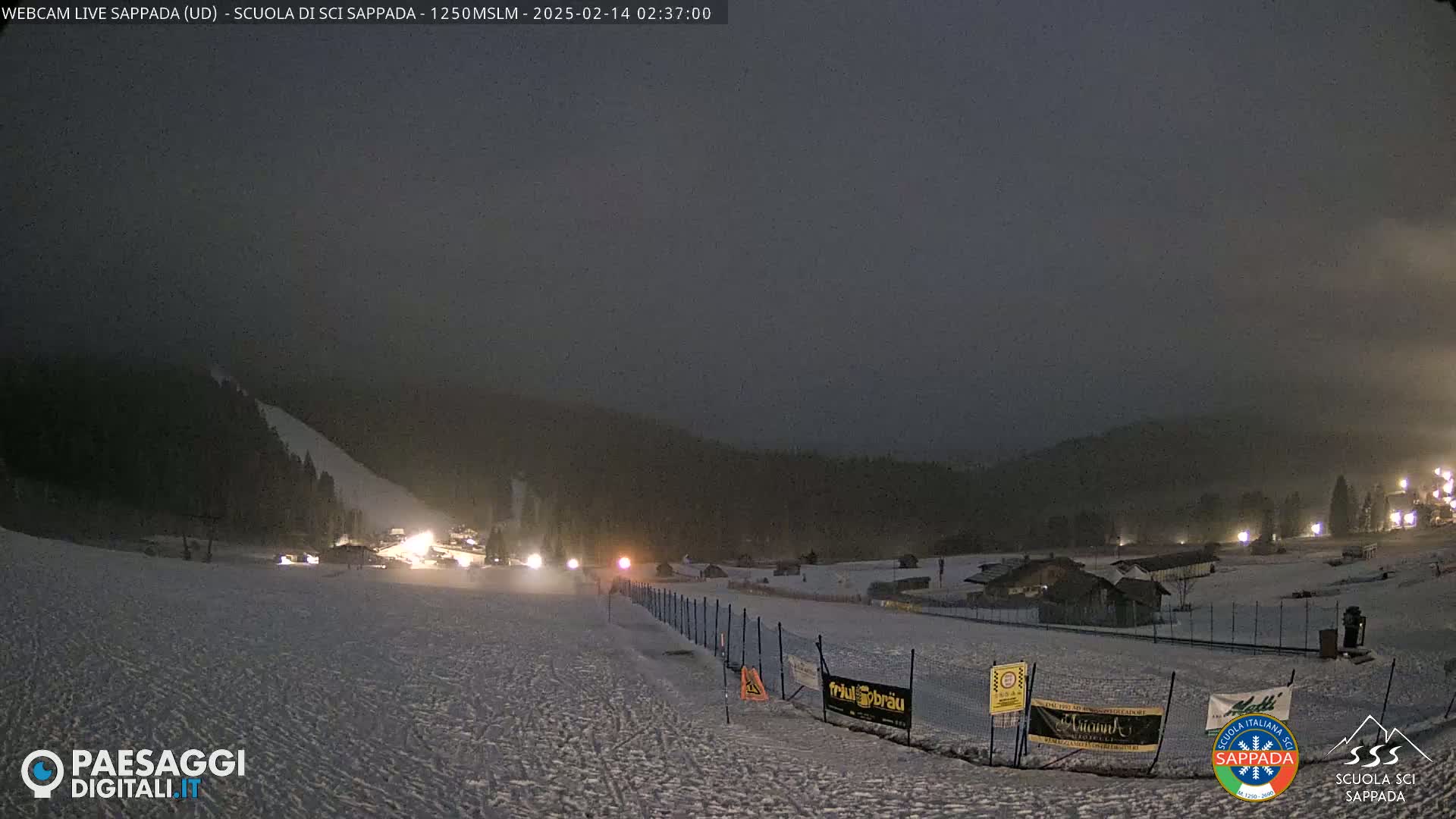 A nighttime view of a snow-covered ski slope with several lights visible, under a hazy, dark sky.