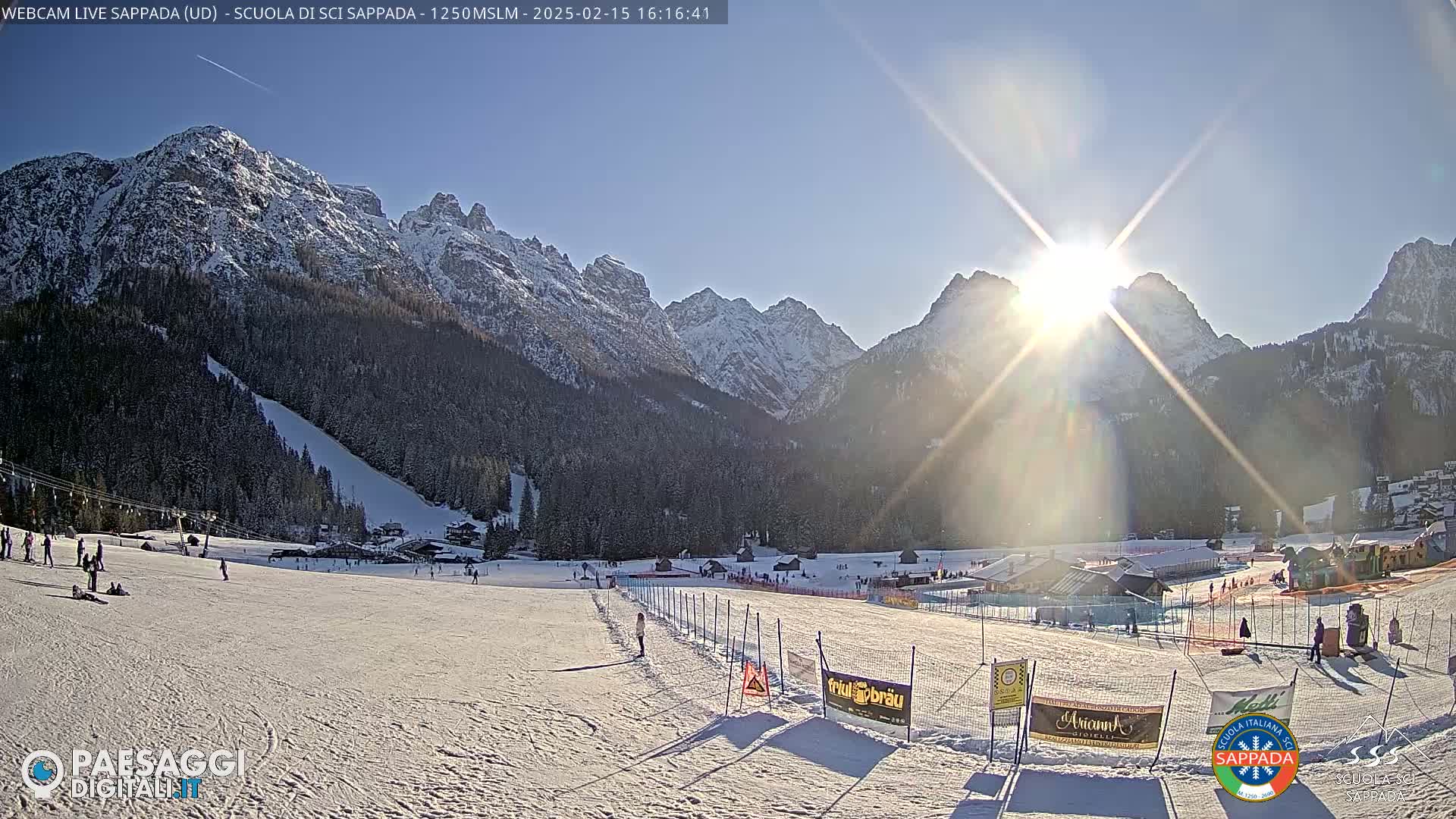 A sunny day at a snow-covered ski resort nestled in a valley between snow-capped mountains.