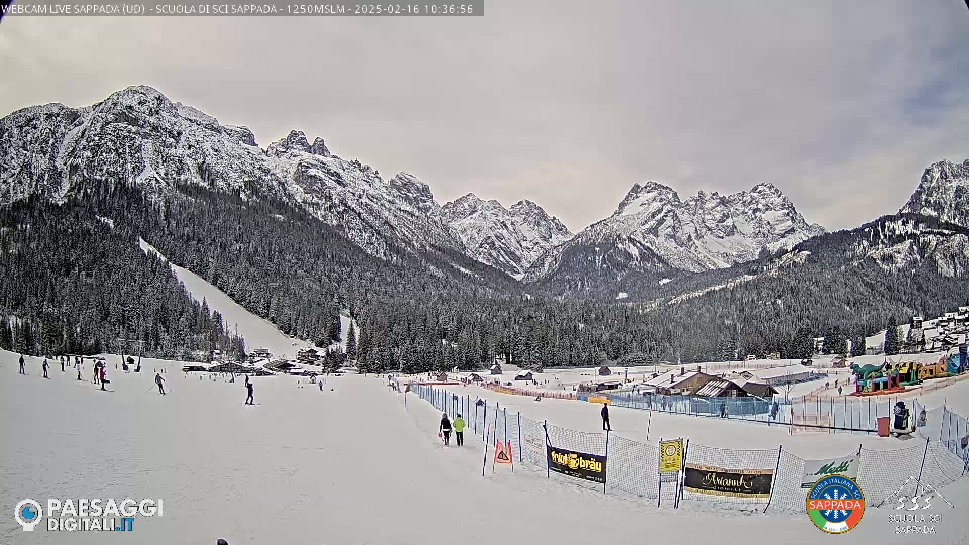 A snowy ski slope with several skiers and a mountain range covered in snow under an overcast sky.