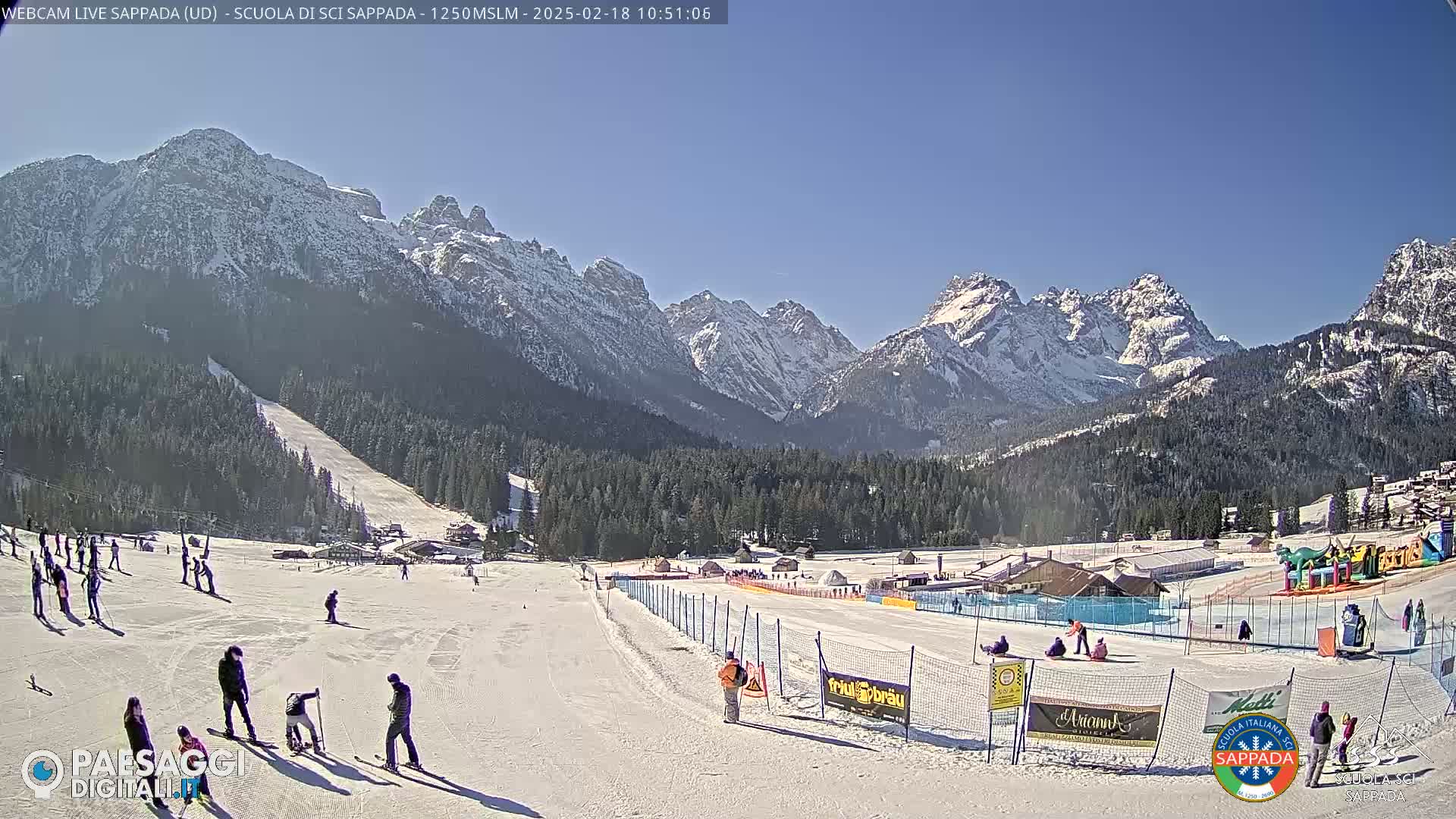 A sunny day at a snow-covered ski resort in the mountains, with skiers and snowboarders enjoying the slopes.