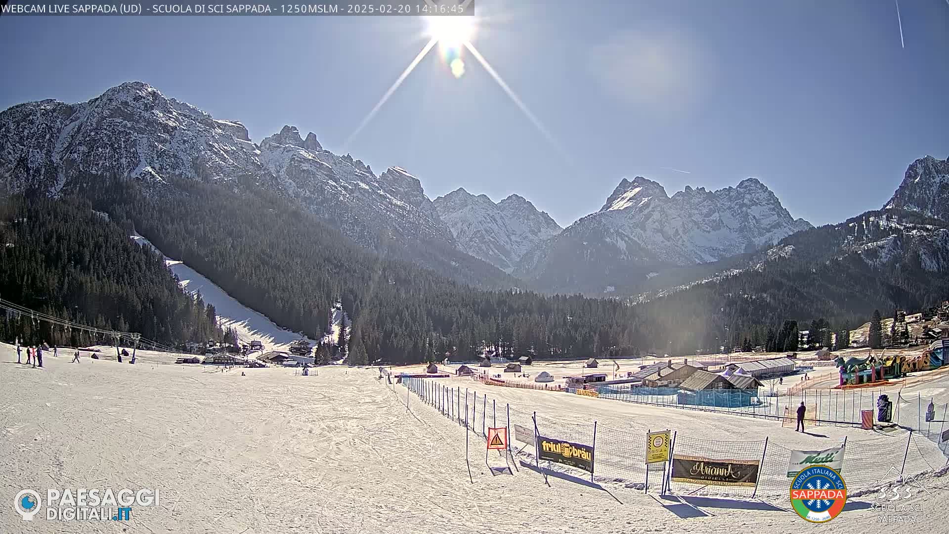 A sunny, snow-covered ski slope is nestled in a valley between snow-capped mountains.
