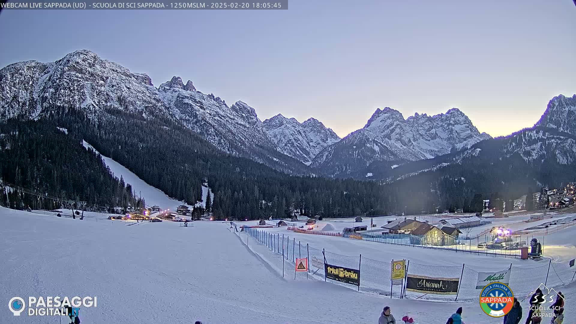 A snow-covered ski resort nestled in a valley between snow-capped mountains at dusk.