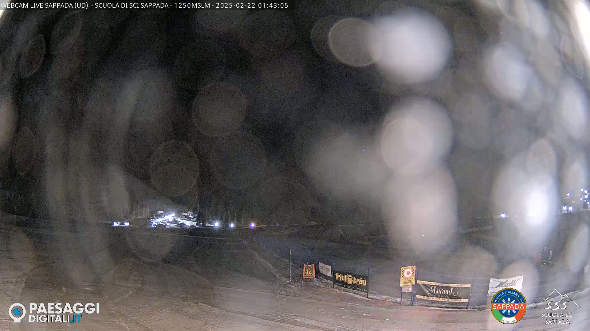 A nighttime, snowy scene shows blurry lights from vehicles on a road, obscured by what appears to be blowing snow or dust.