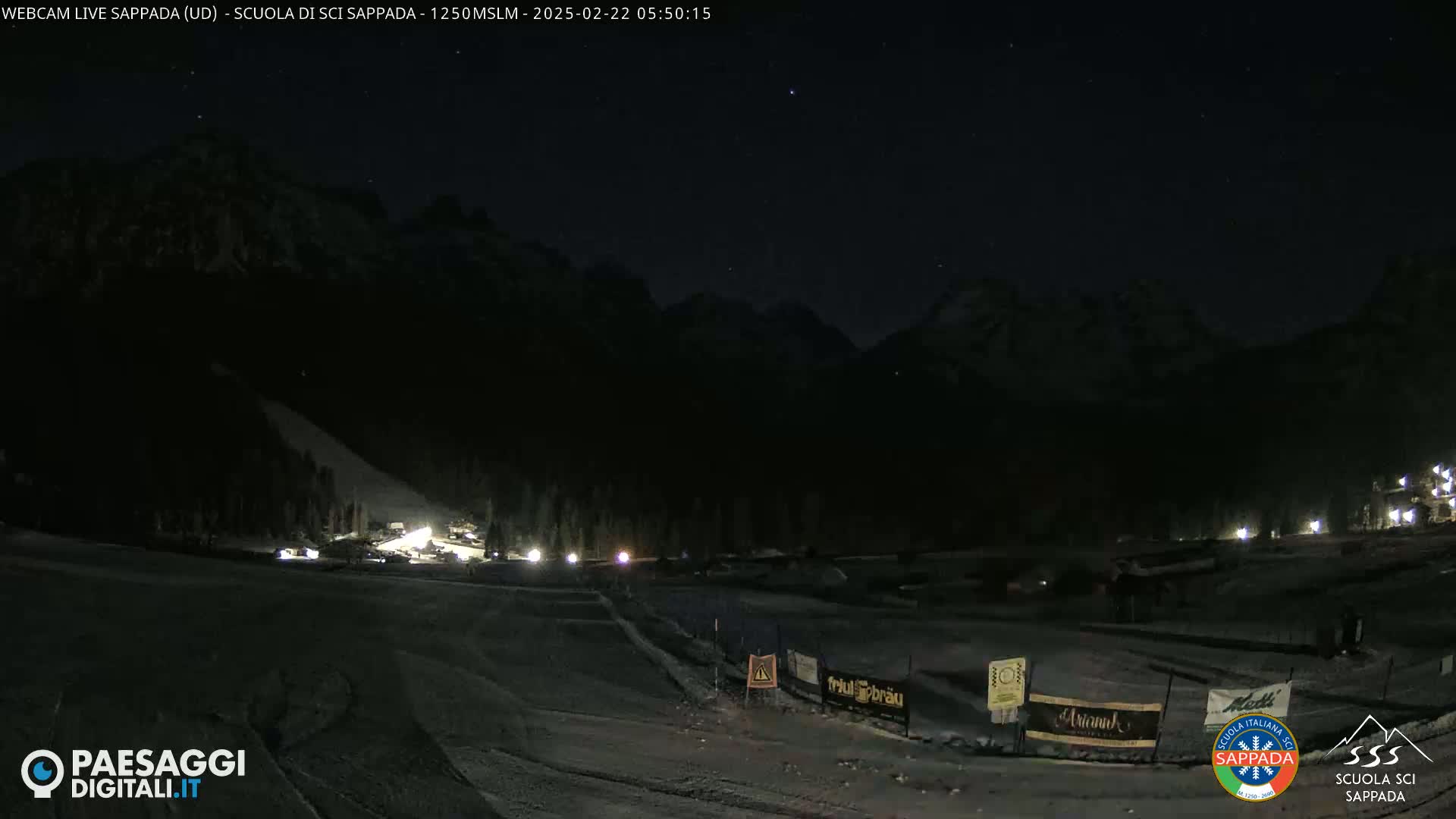A nighttime view of a snow-covered ski slope at the base of dark mountains under a clear, starry sky.