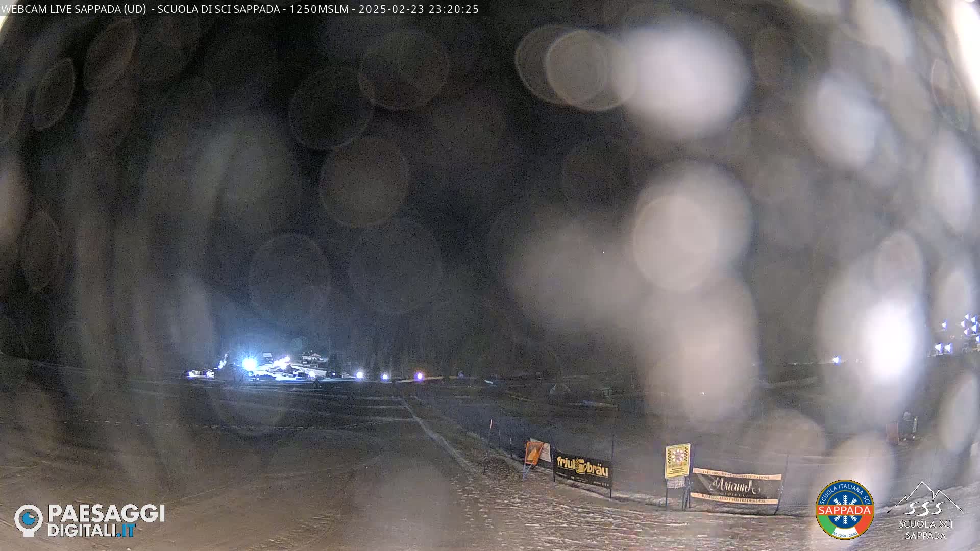 A nighttime view of a snowy, dimly lit area with blurry foreground, possibly due to weather conditions such as snow or rain.