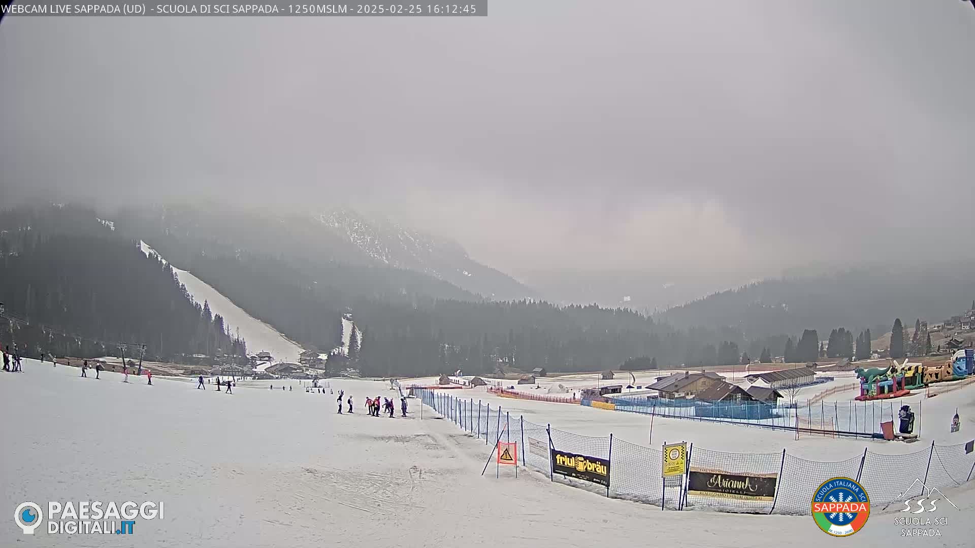 A snowy ski slope with a few skiers and a hazy, overcast sky over a mountainous landscape.