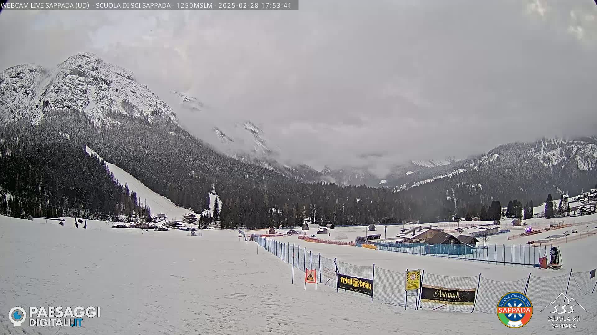 A snow-covered ski slope stretches toward snow-capped mountains under an overcast sky.