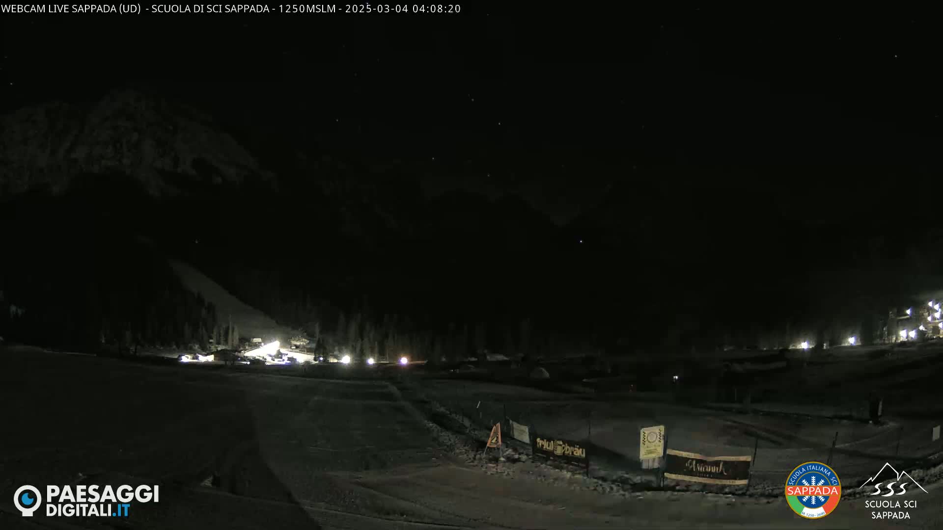 A nighttime view of a snow-covered ski slope with a few lights visible at the bottom, and a dark mountain in the background under a clear, starlit sky.