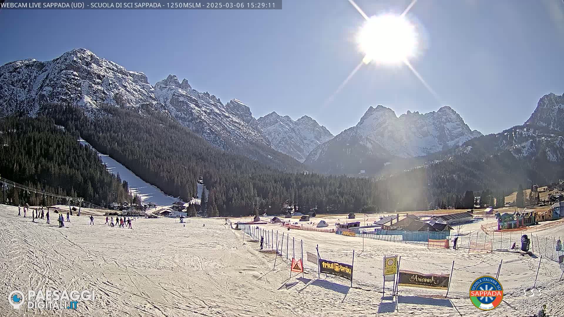 A sunny day at a snow-covered ski resort nestled in a valley between snow-capped mountains.