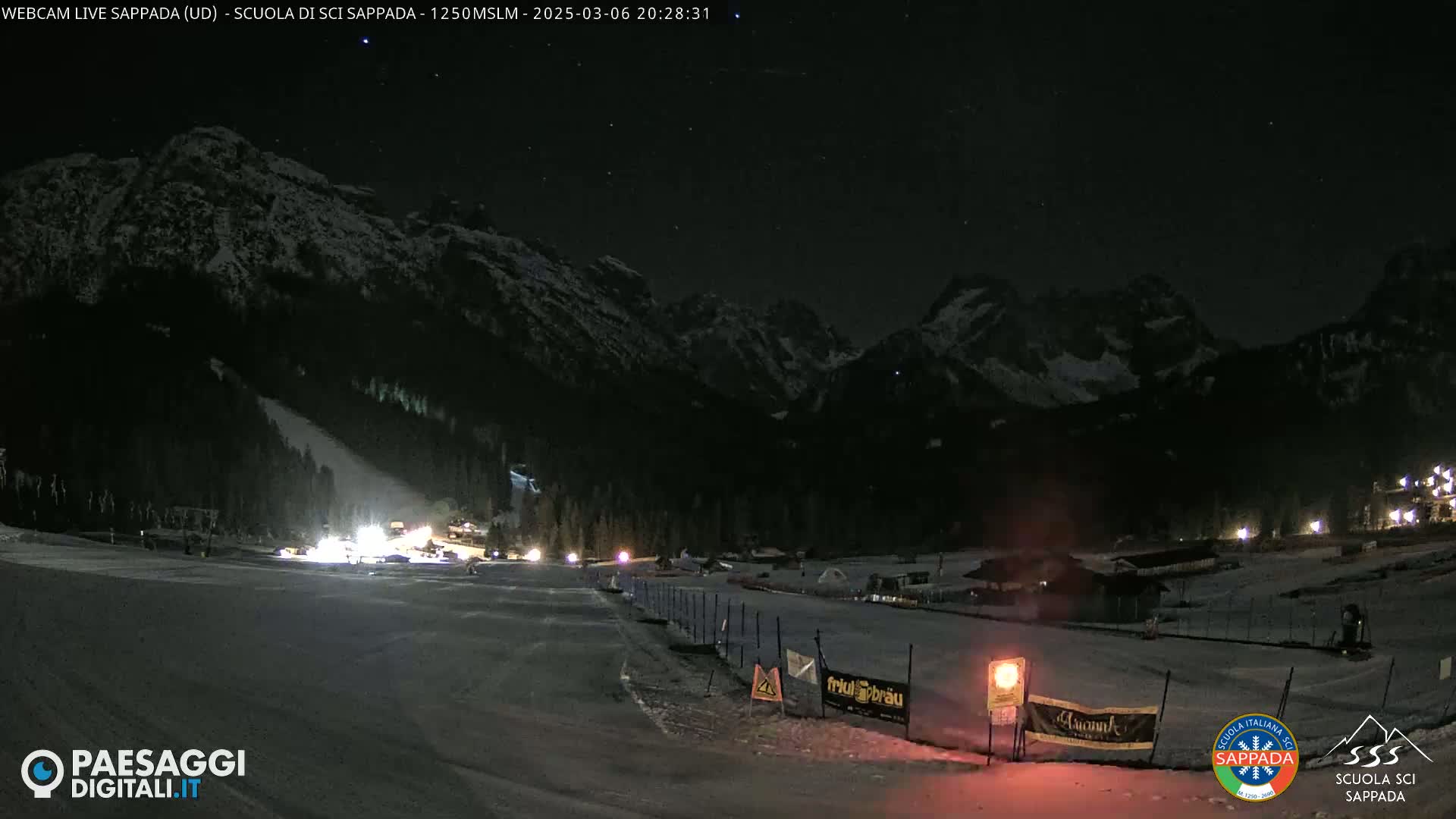 A nighttime view of a snow-covered ski resort nestled among dark, snow-dusted mountains under a clear, starry sky.