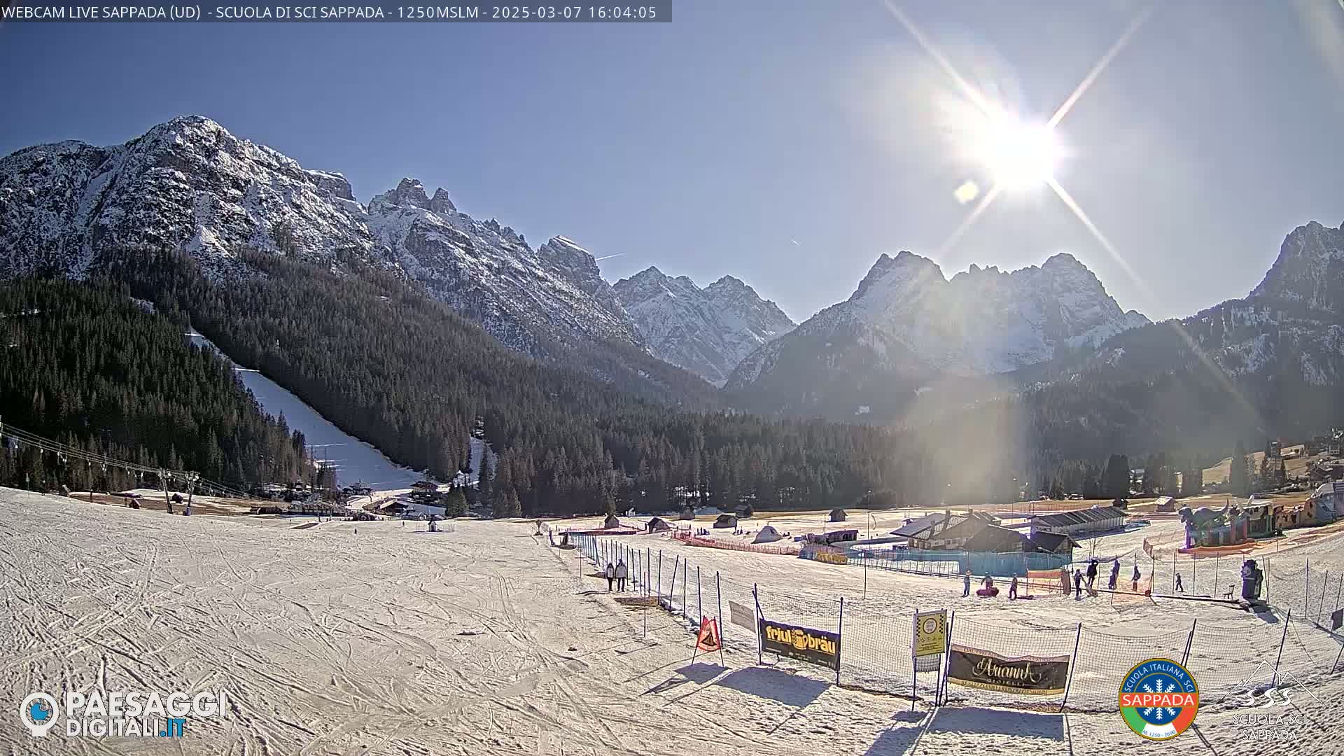 A sunny day on a snow-covered ski slope, with a backdrop of snow-capped mountains.
