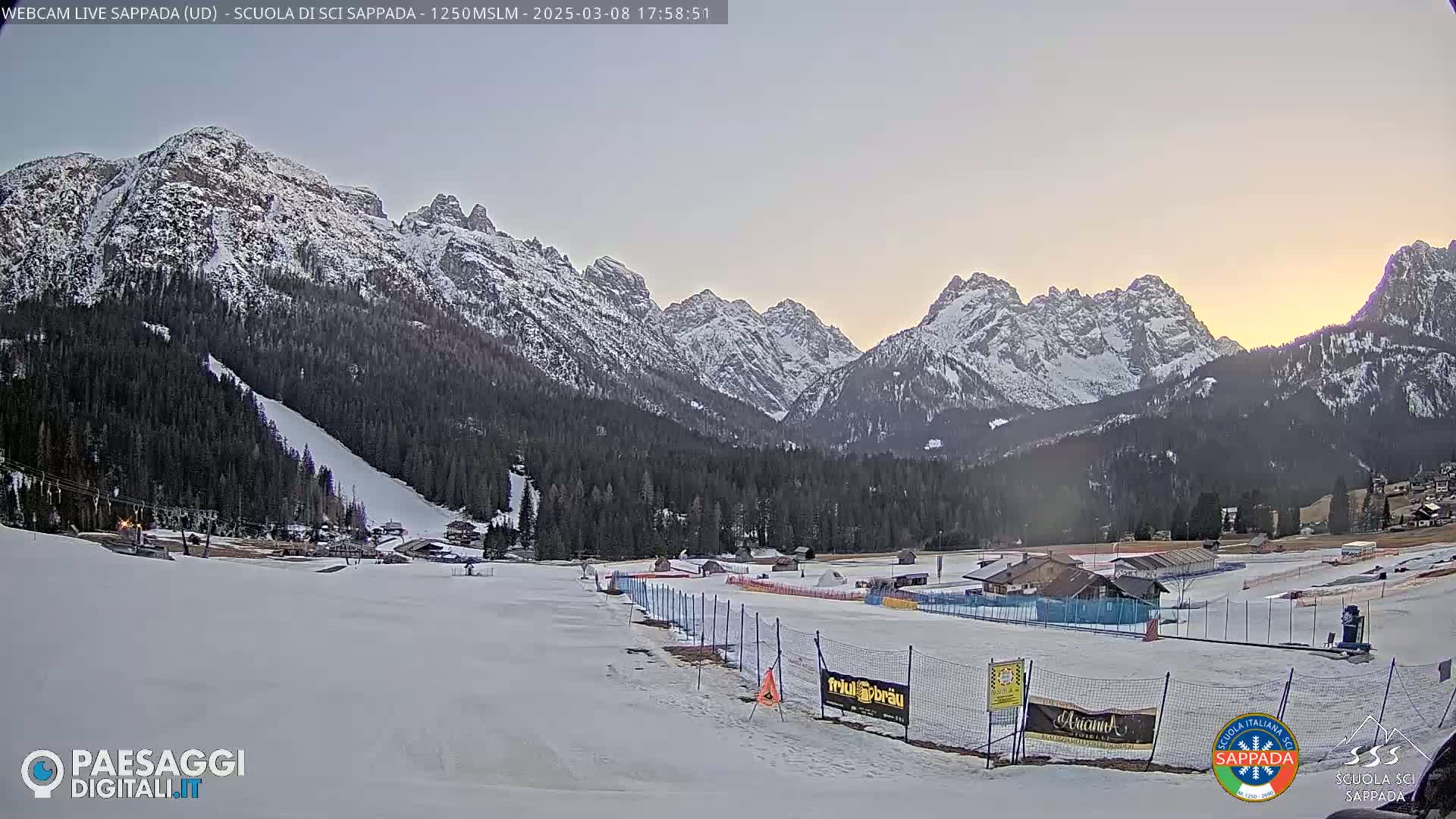 A snow-covered ski resort valley is nestled between snow-capped mountains under a twilight sky.
