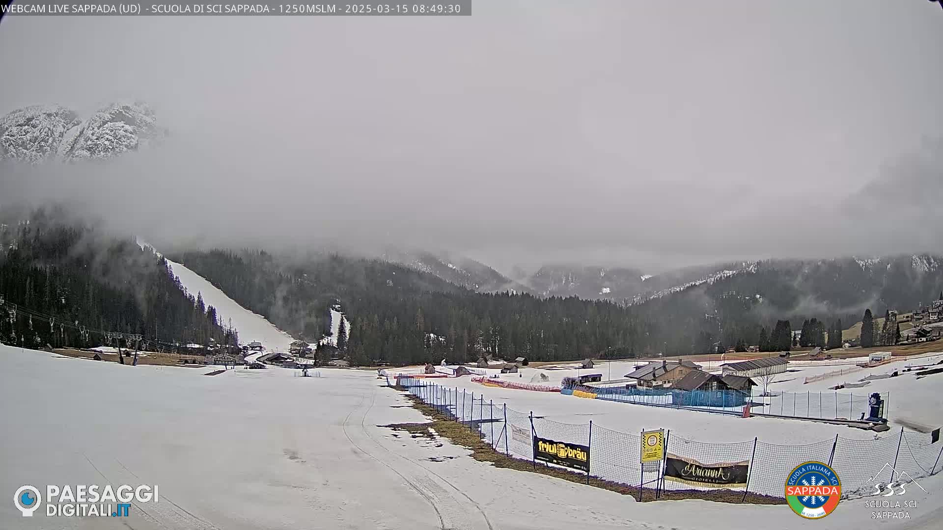 A snow-covered ski slope and surrounding mountain landscape are visible under a foggy, overcast sky.