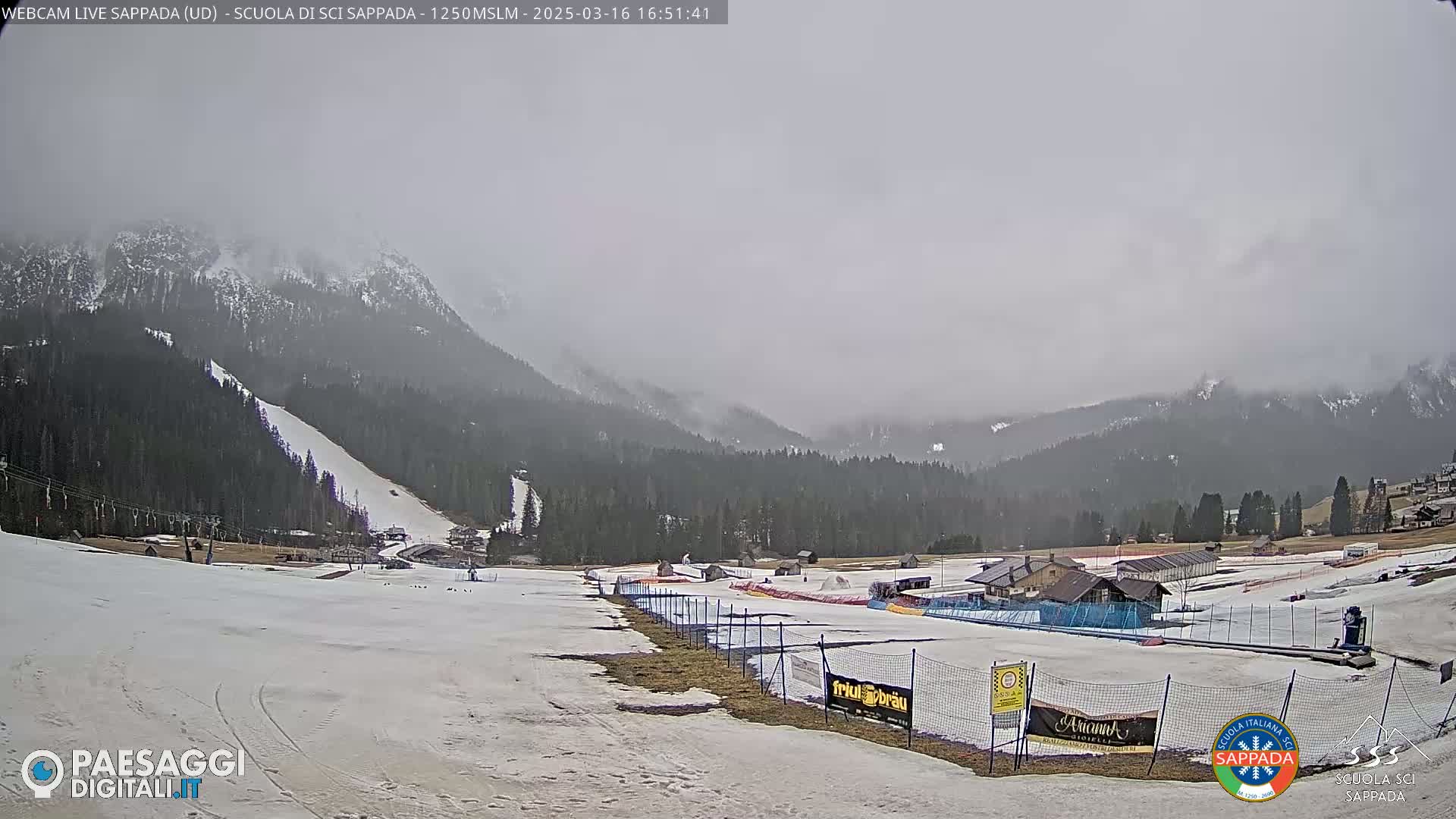 A snow-covered ski slope and surrounding mountainous terrain are visible under an overcast sky.