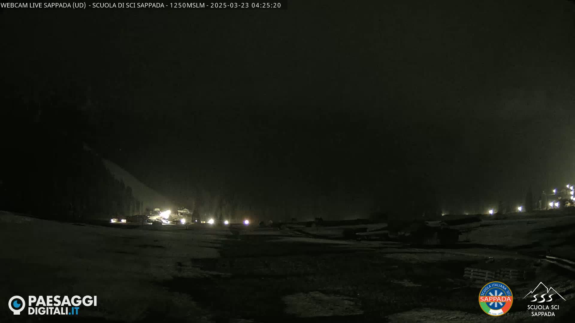 A nighttime, snow-covered scene with dimly lit buildings and vehicles under a dark, cloudy sky.