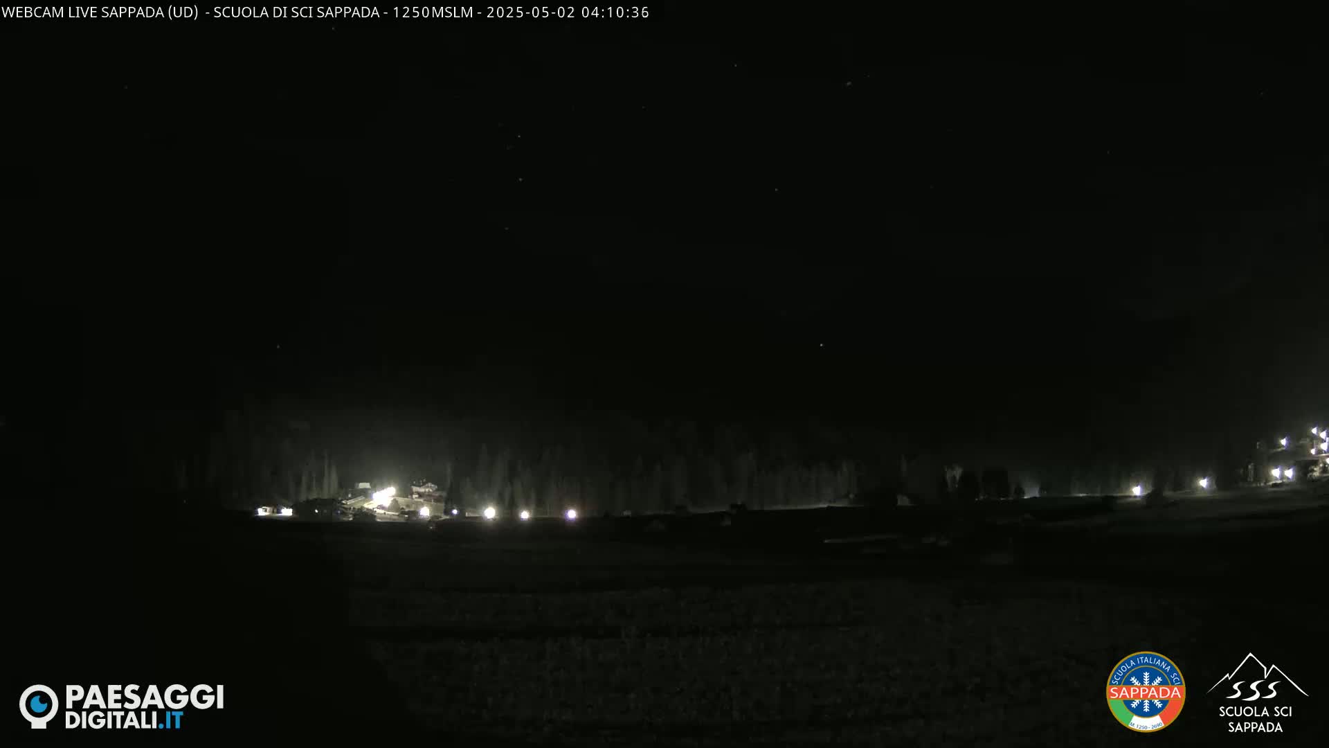A dark, nighttime scene shows a snow-covered landscape with a few distant lights.