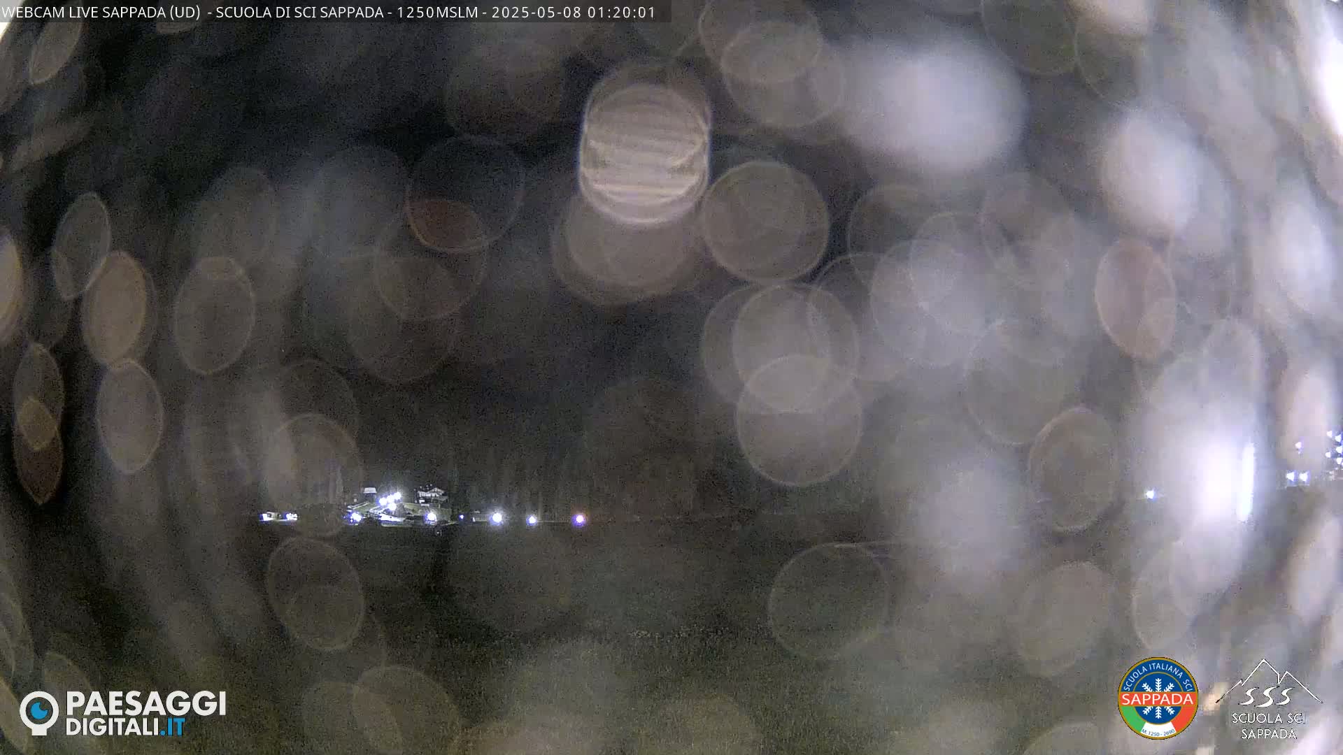A nighttime, blurry view of a dimly lit area with scattered lights, possibly seen through rain-covered glass.