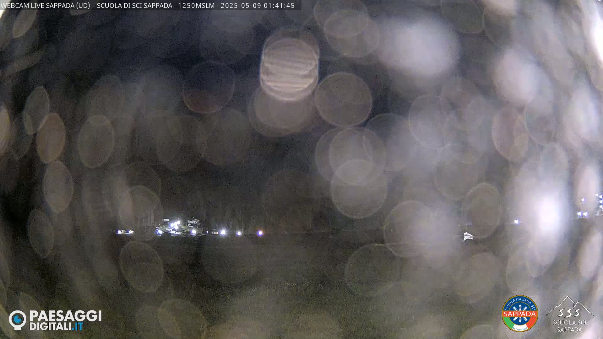 A nighttime outdoor scene is visible through a rain-covered surface, showing blurry lights in the distance.