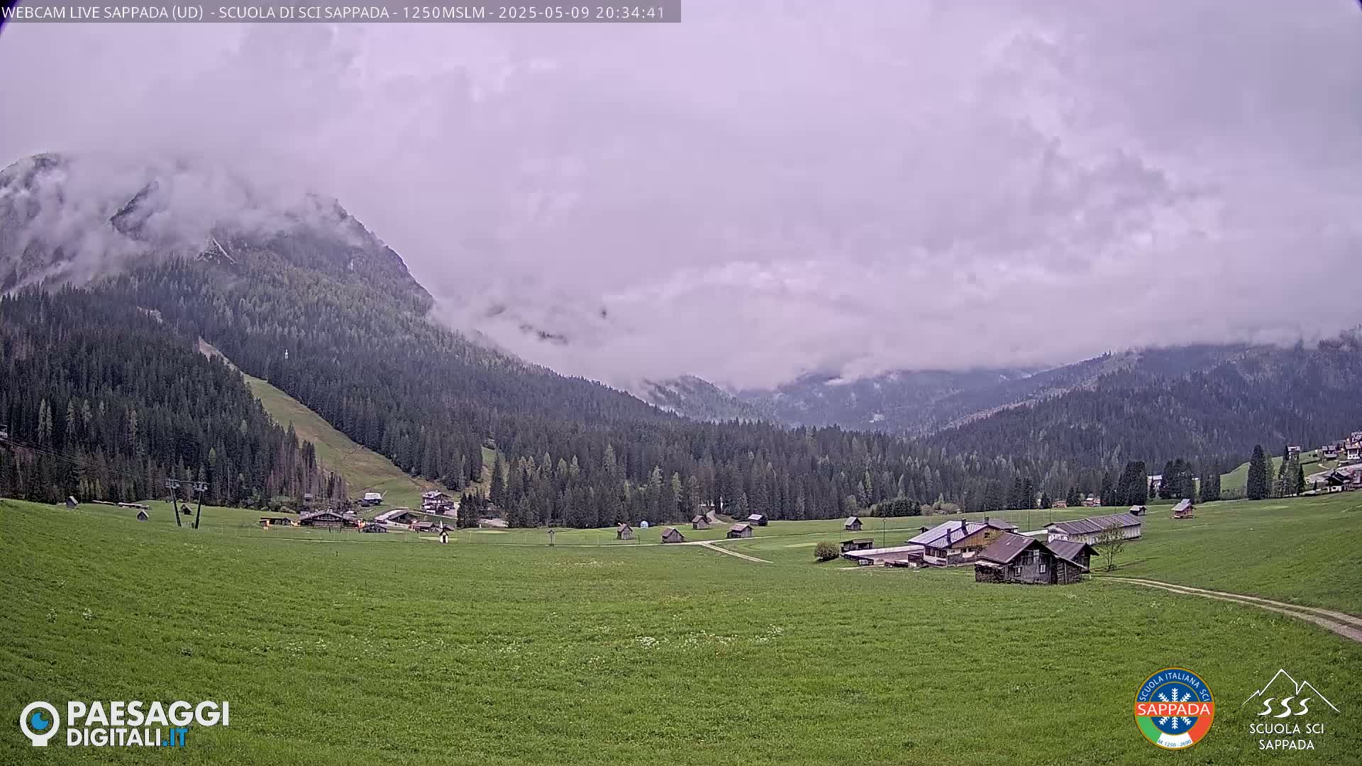 A mountain village nestled in a verdant valley, shrouded in a cloudy, overcast sky.