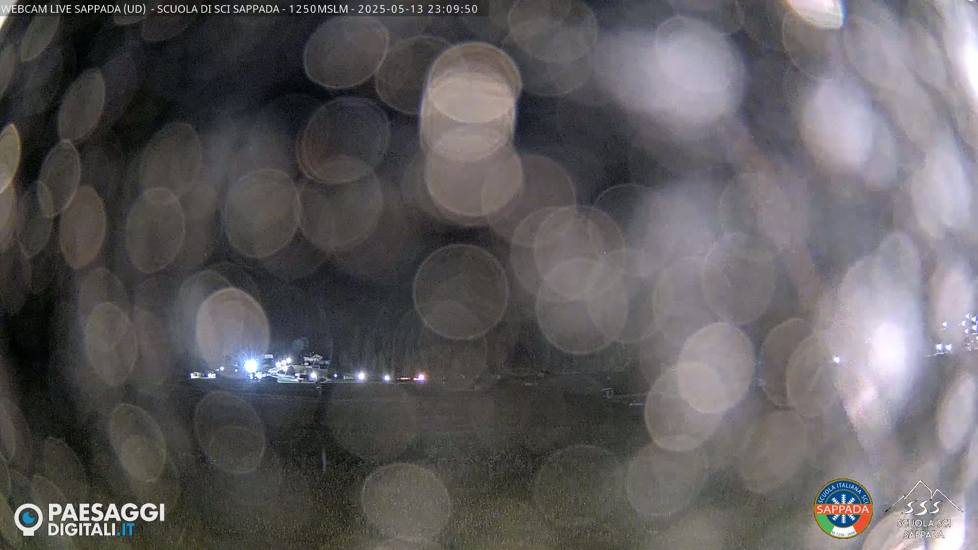 A nighttime, blurry view of a dark landscape with a few distant lights, seen through a rain-covered surface.