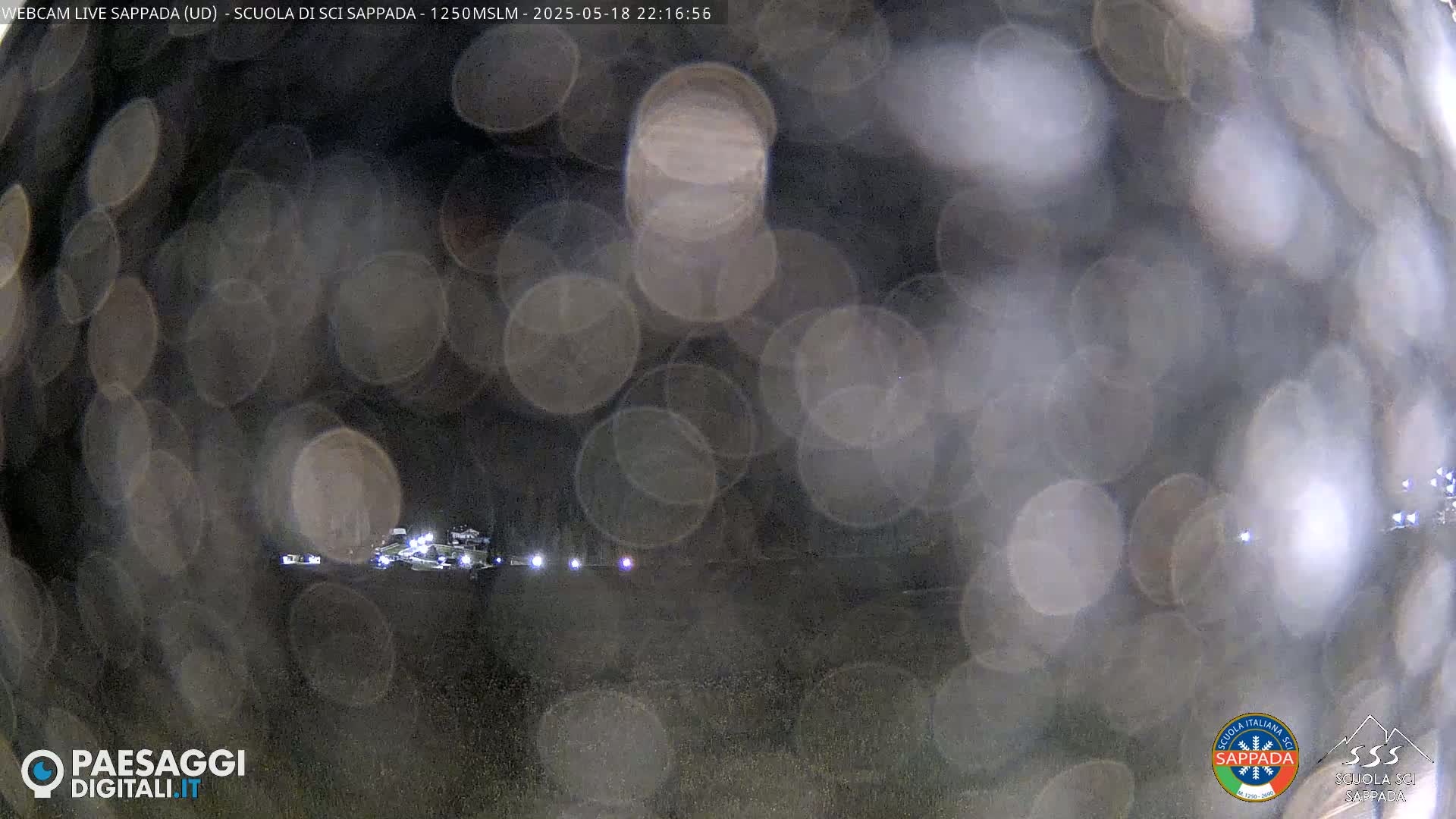 A blurry nighttime image shows a dark landscape with indistinct vehicles and lights, viewed through a rain-covered surface.