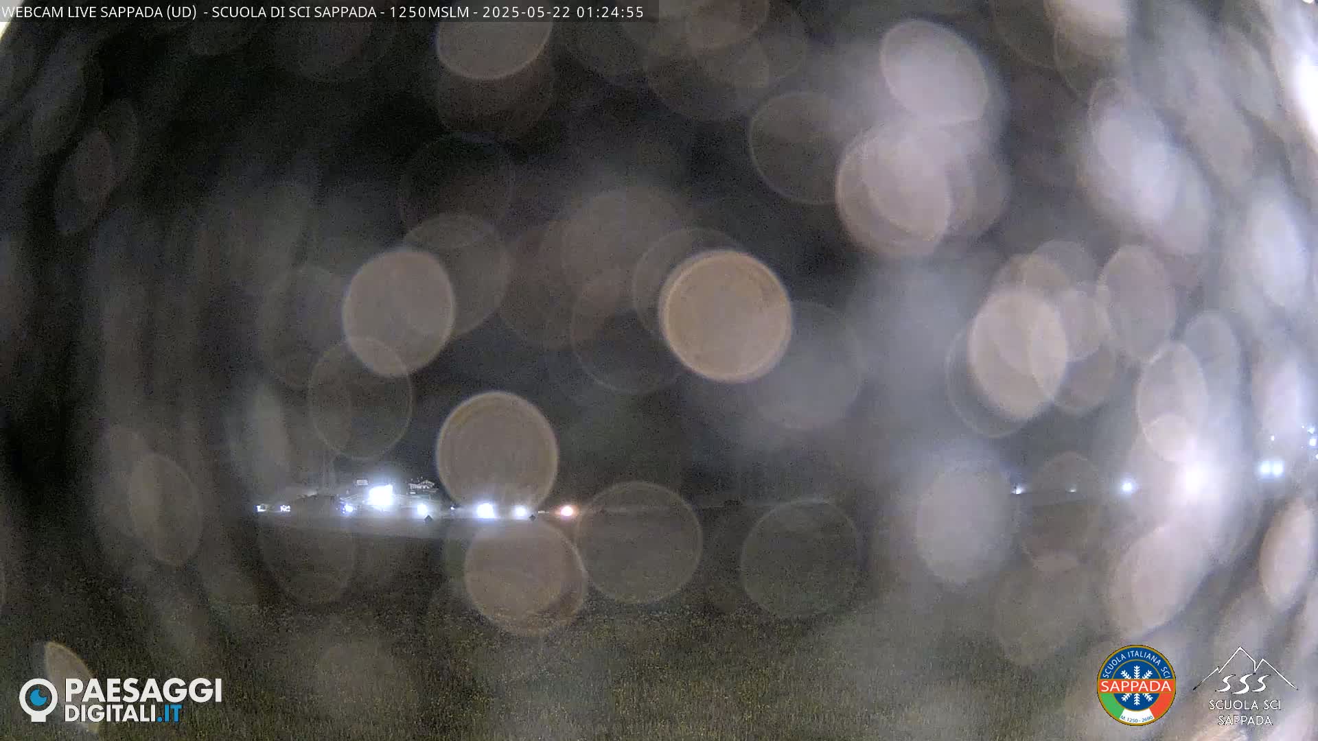 A nighttime outdoor scene showing blurred lights of vehicles in the distance through a rain-covered window.