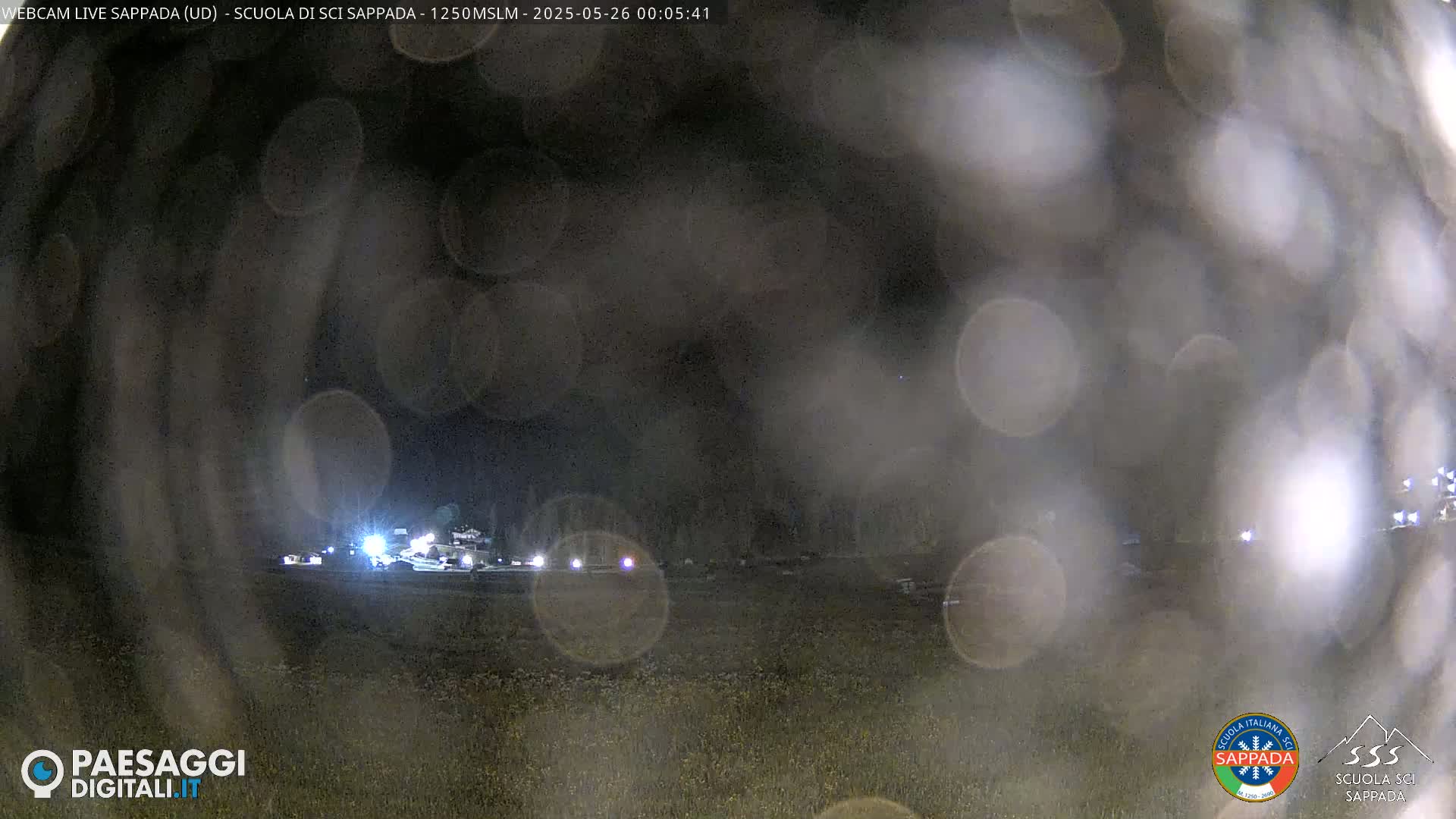 A nighttime, blurry view of a sparsely lit area of land, possibly a parking lot or field, with some lights visible in the distance.