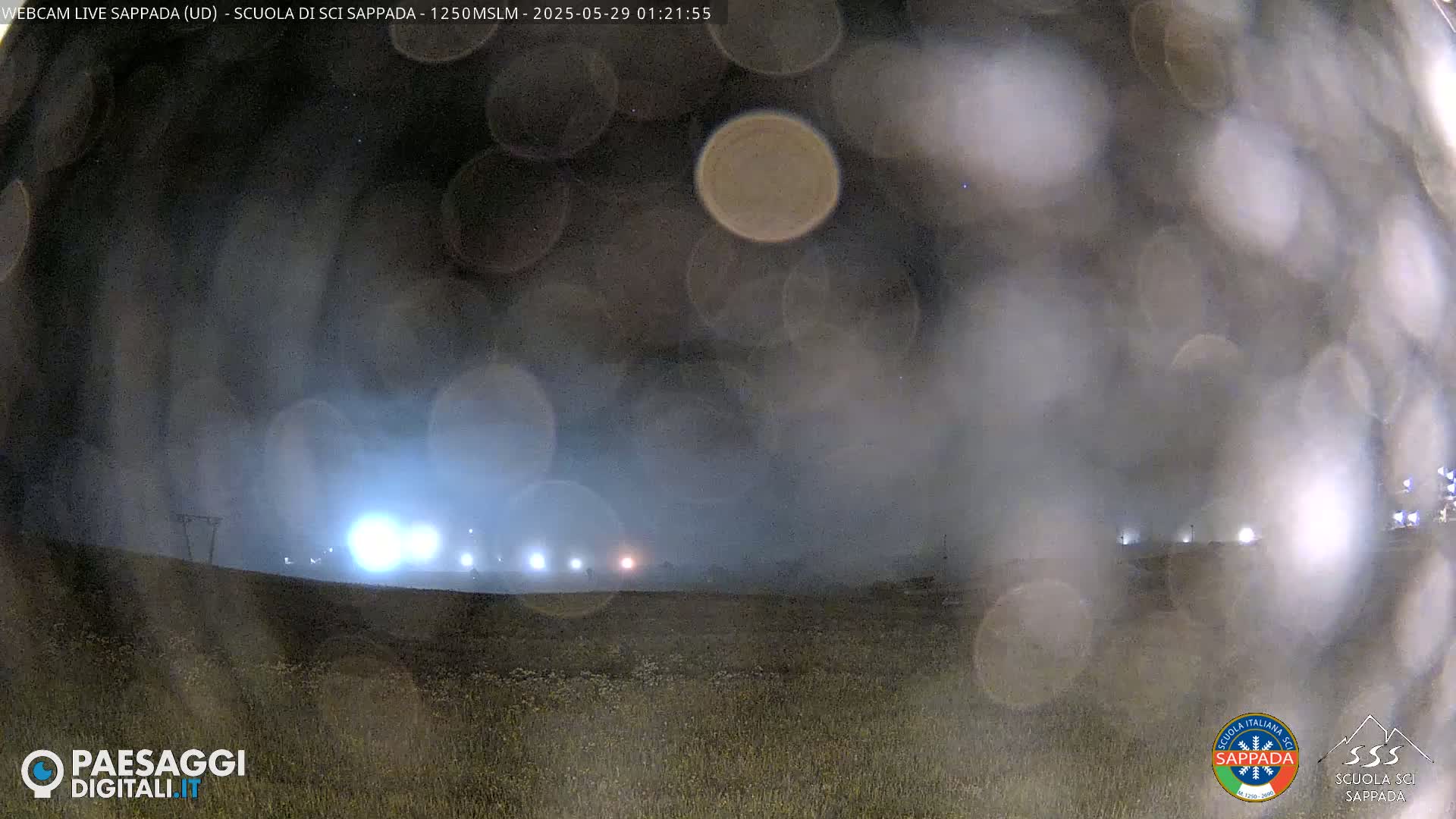 A nighttime, hazy view of a field with distant lights, possibly from buildings, visible through a somewhat blurry lens.