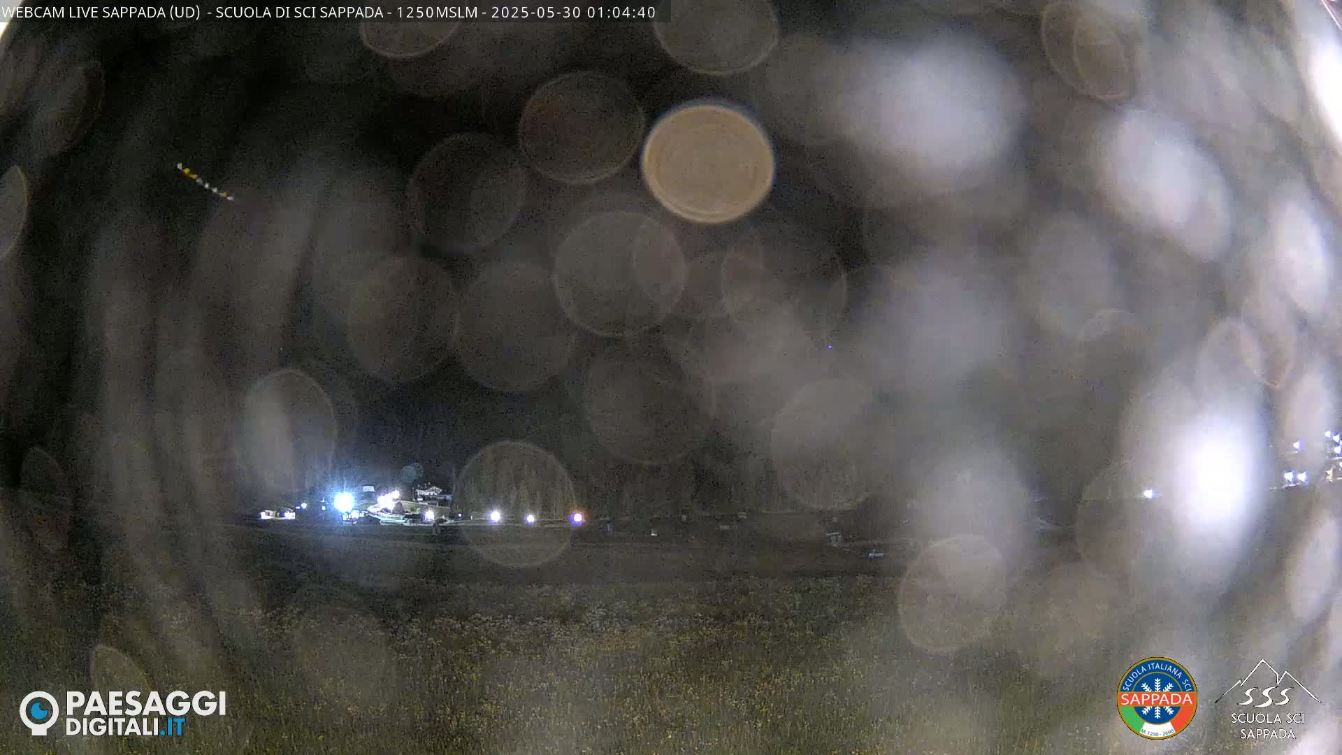 A nighttime, blurry view of a field with distant lights, possibly vehicles, under a dark sky with many out-of-focus light sources obscuring the view.
