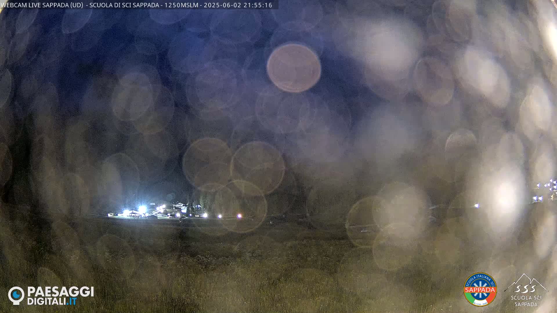 A nighttime, blurry view of a lighted building complex, possibly a ski resort, obscured by rain or fog.
