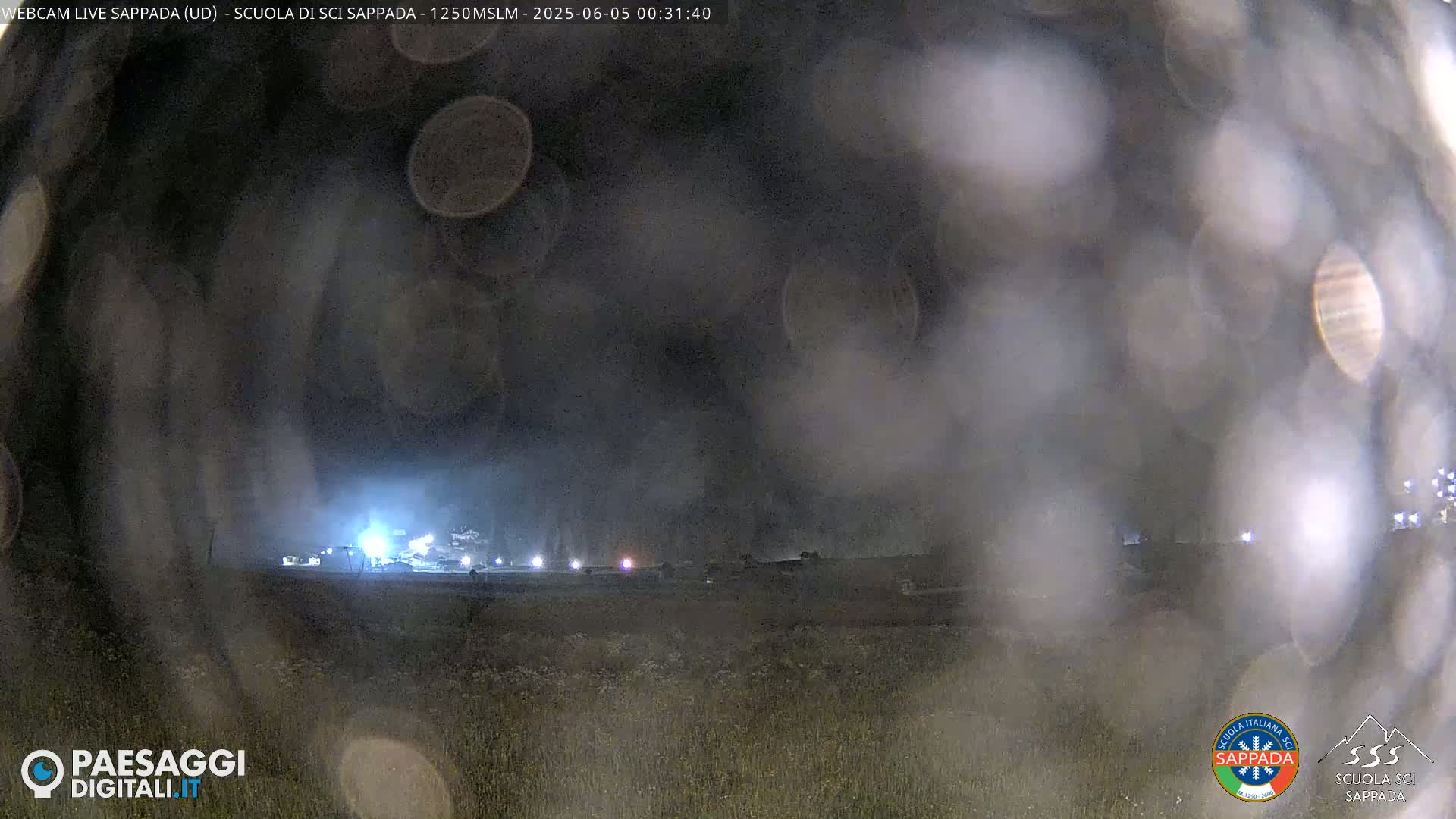 A nighttime, hazy view of dimly lit buildings and structures in a field.