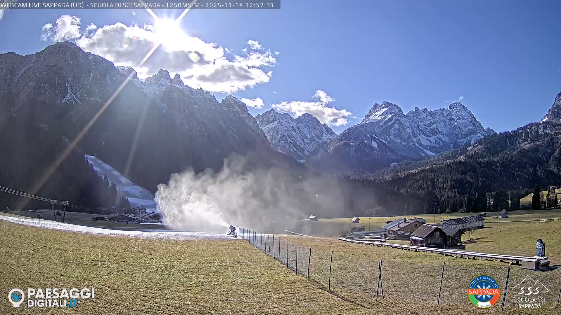 A heavily blurred night-time image shows brightly lit snowmaking machinery on a ski slope, with low visibility caused by dense fog or heavy snowfall and moisture on the camera lens.