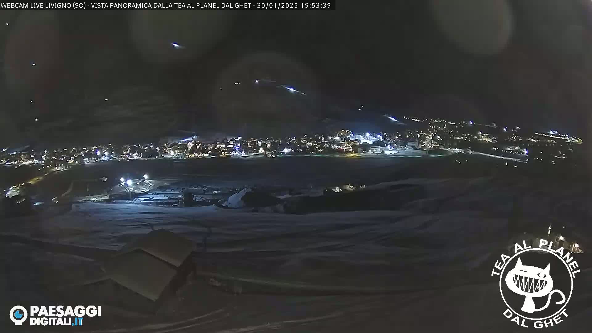 A nighttime, panoramic view of a snow-covered town illuminated by lights, with a clear sky showing a few distant lights.