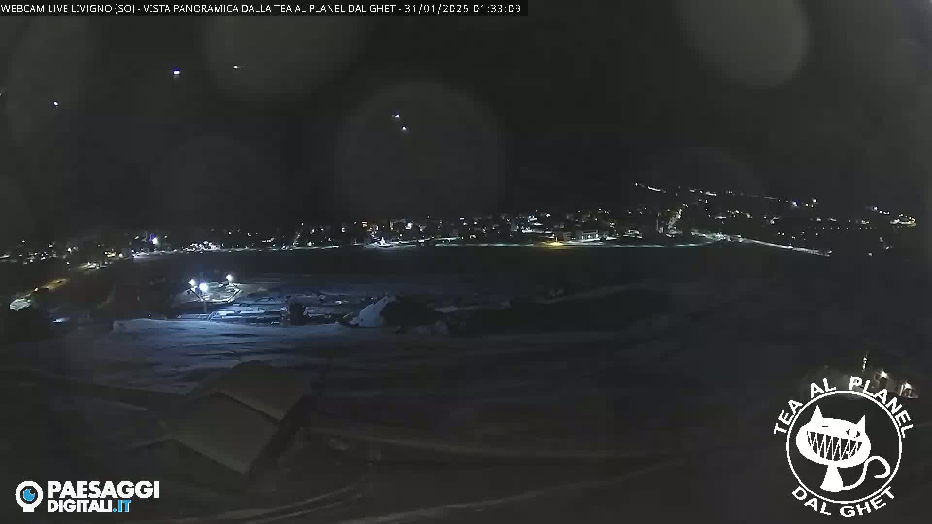 A nighttime, snowy panoramic view of a town illuminated by scattered lights under a dark sky.