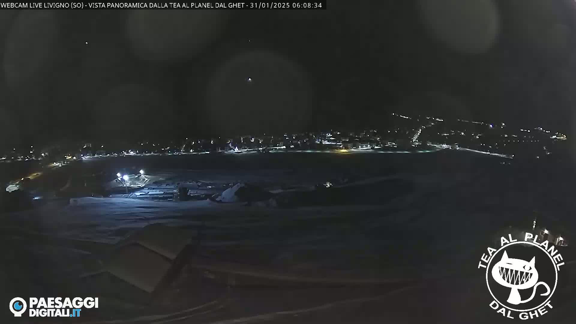 A nighttime, snowy landscape shows a town with faint lights in the distance under a dark sky.