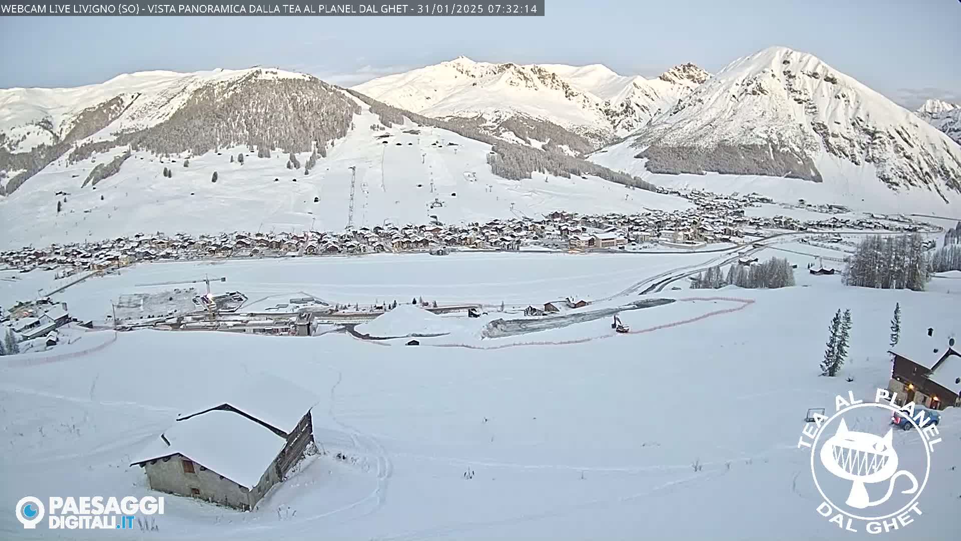 A snow-covered village nestled in a valley between snow-capped mountains under a clear sky.