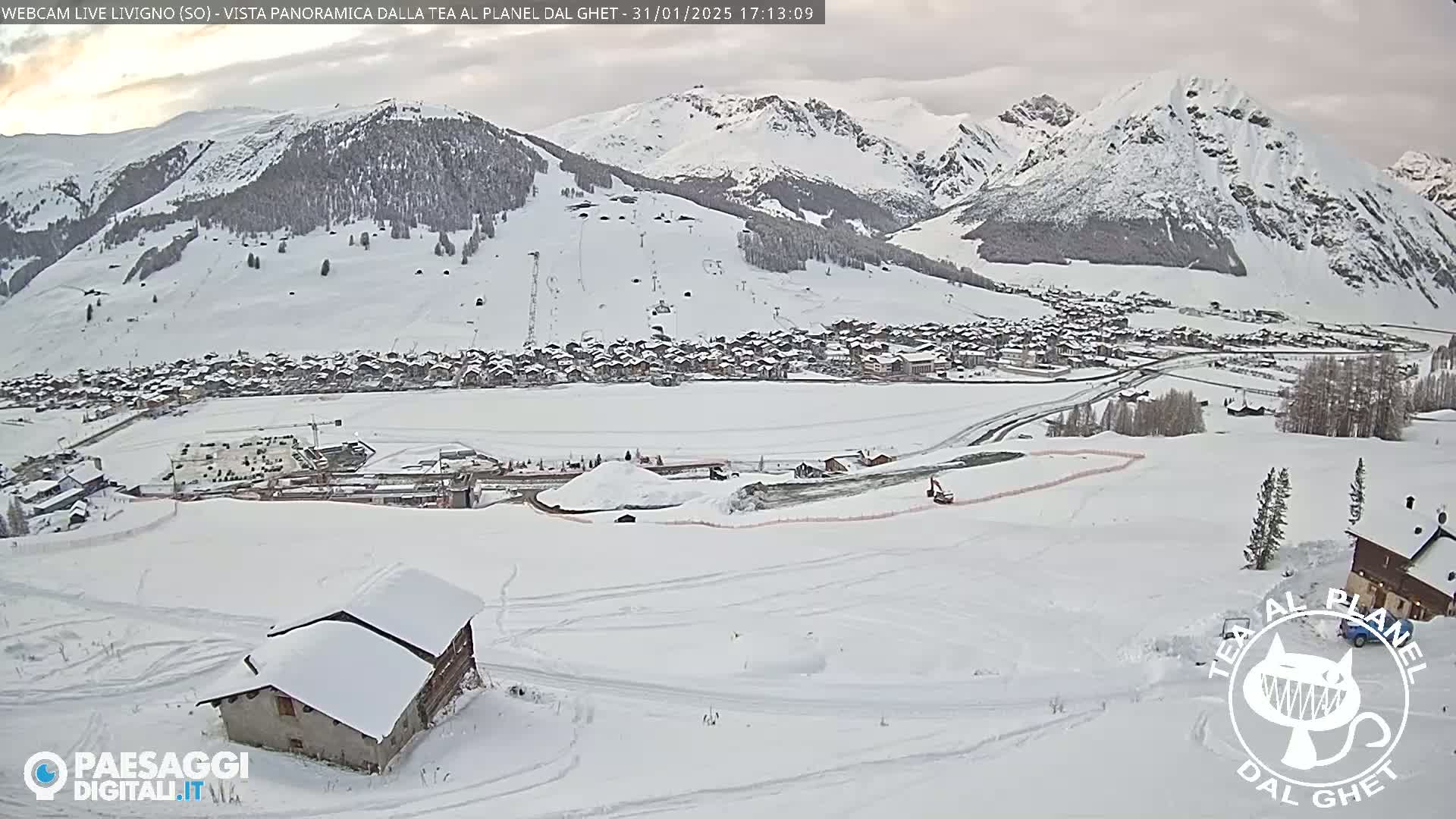 A snow-covered village nestled in a valley between snow-capped mountains, under an overcast sky.