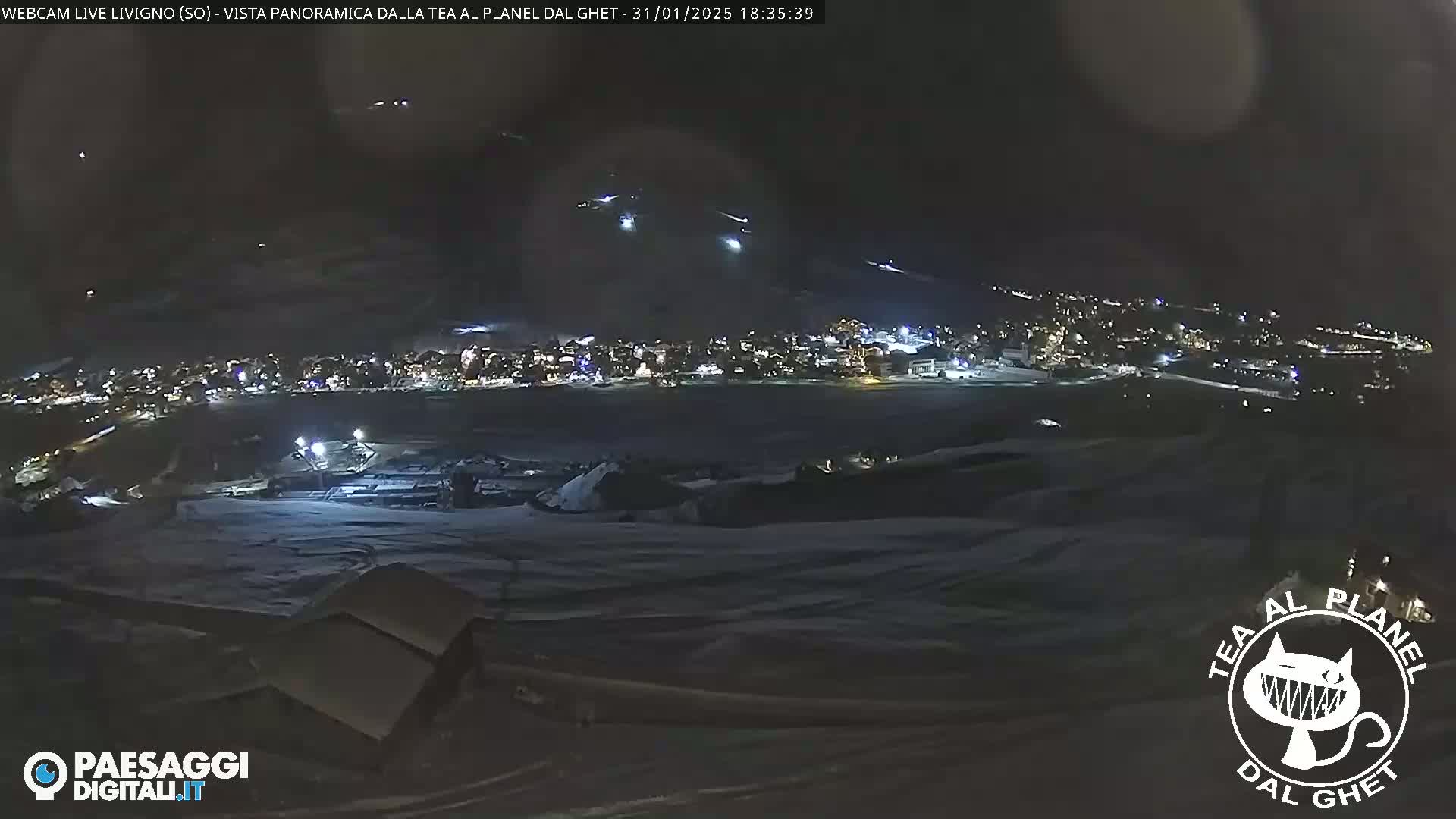 A nighttime, snow-covered landscape shows a town illuminated below, with several lights moving in the sky above.