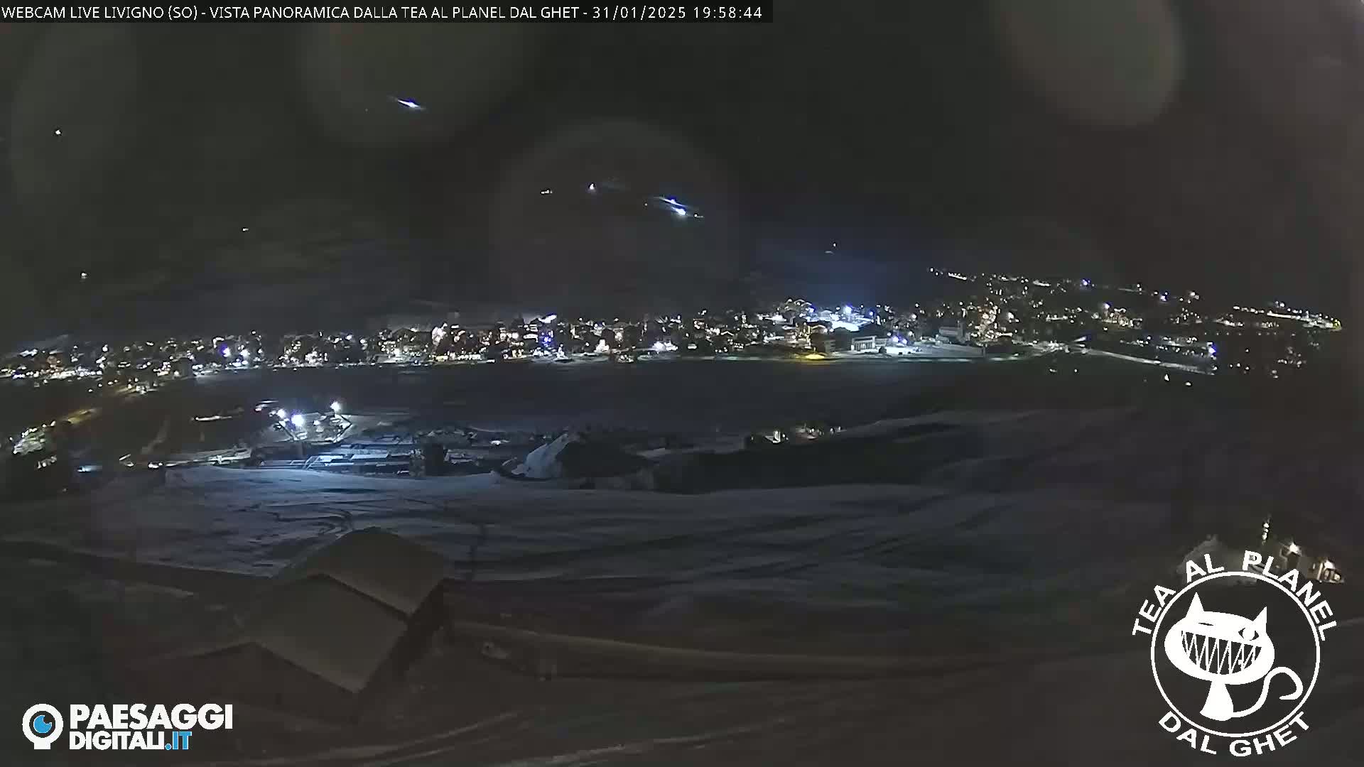 A nighttime, snowy landscape shows a distant, illuminated town under a dark sky with several visible shooting stars.