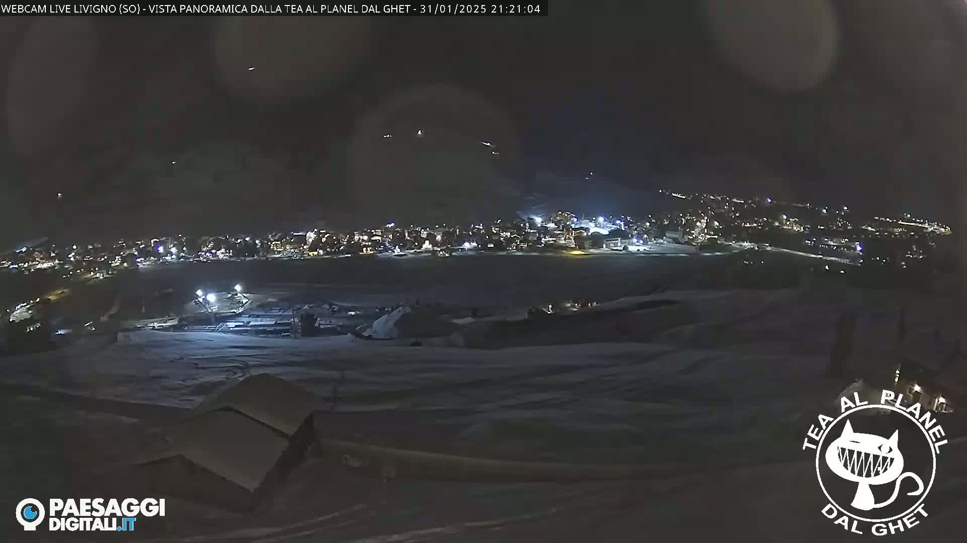 A nighttime, snowy, panoramic view of a town with lights illuminated against a dark sky.